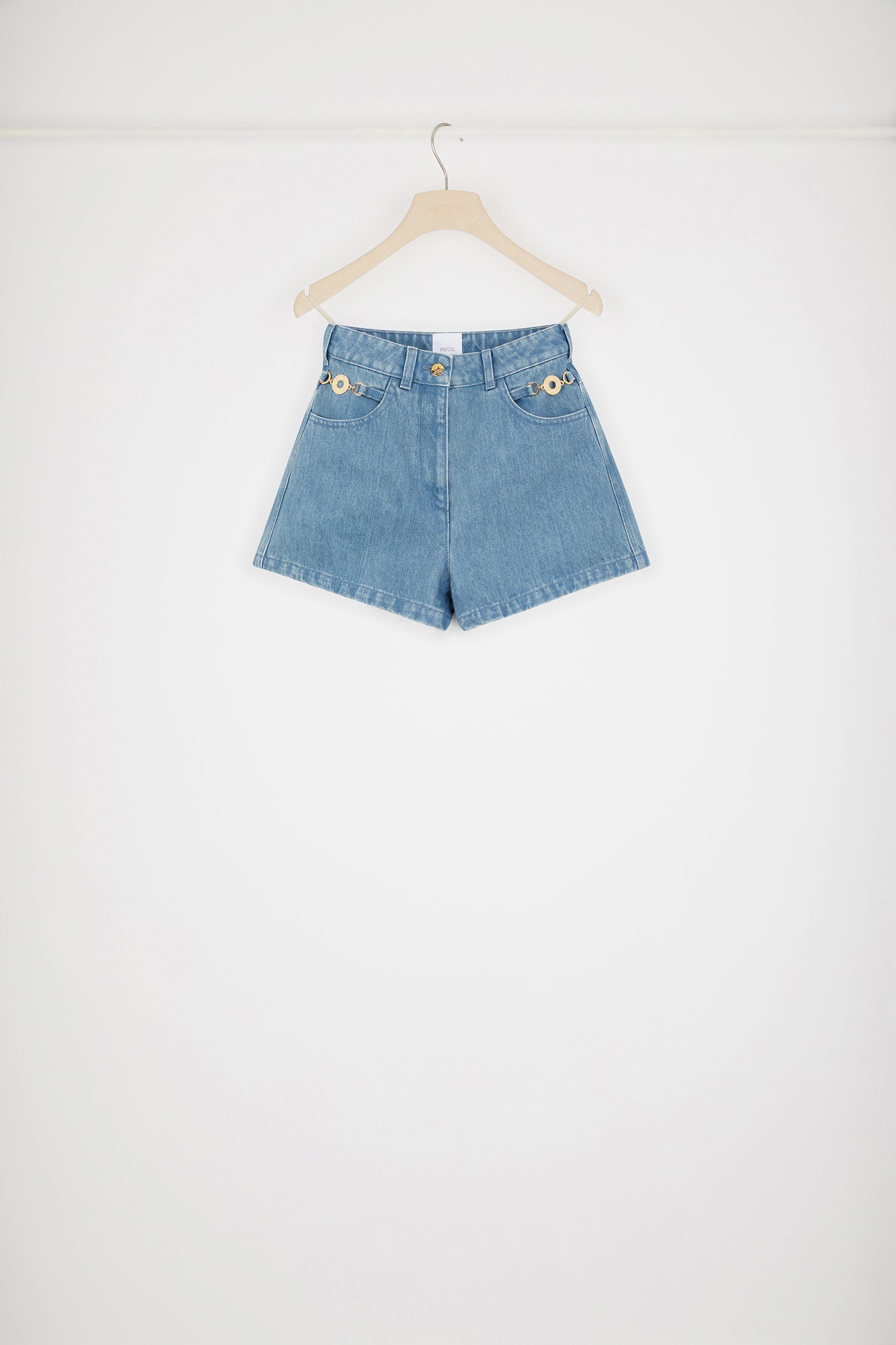 Patou - コットンデニム ミニショートパンツ - Ice Blue - ミニなのに存在感たっぷり。アイスブルーのコットンデニム製ショートパンツ。ハイウエスト。ミニ丈。フロントにゴールドトーンのパトゥ刻印入りメダリオン装飾。フロントにゴールドトーンのパトゥ刻印入りボタン。ベルトループ付き。サイドにポケット。ウエストにパトゥの刺繍。バックにVシーム。