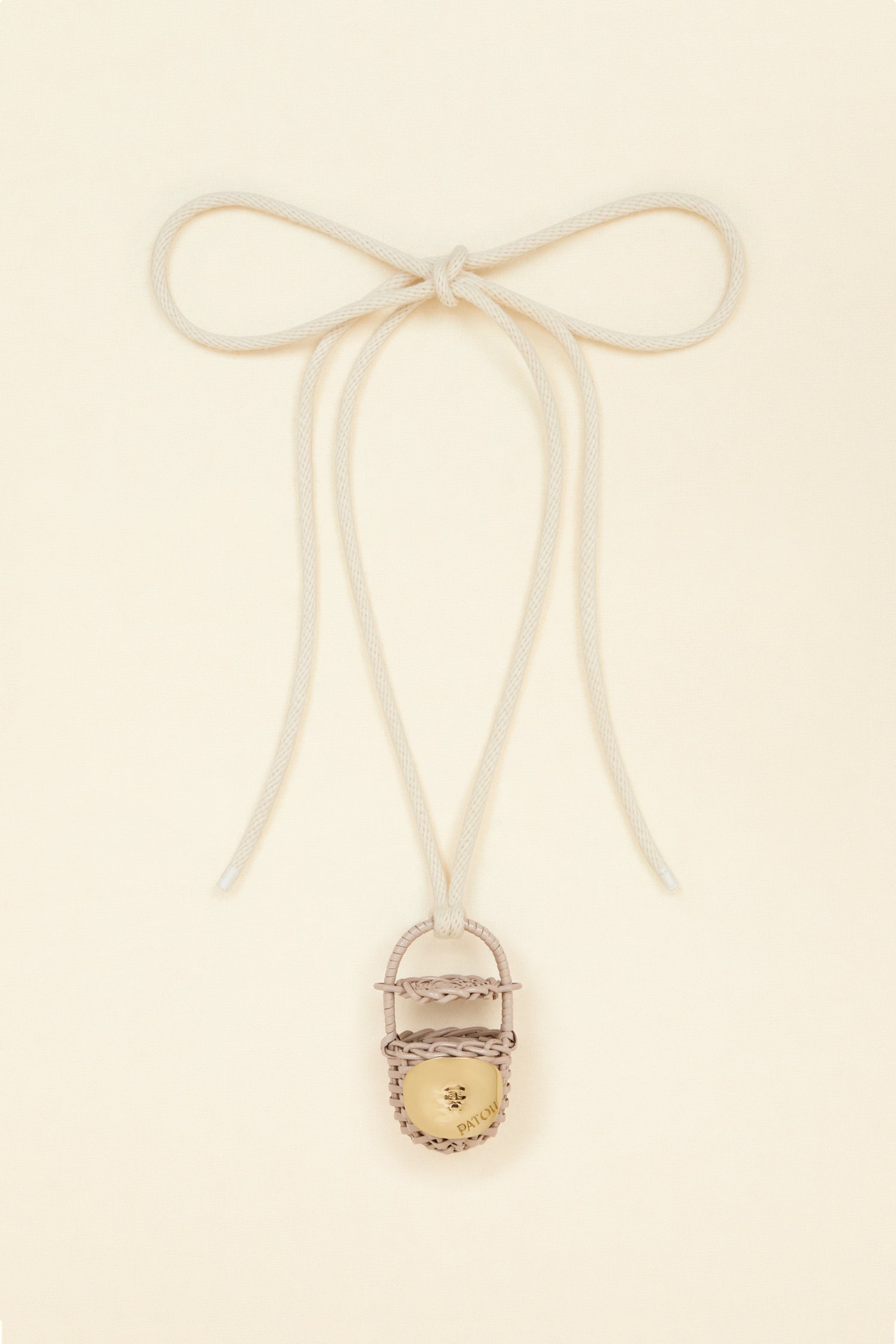 Patou - Bucket bag necklace in wicker - Parchment - A shiny amulet to carry your Patou everywhere with you. Ecru cord necklace with miniature wicker bucket bag pendant in Parchment beige. Top handle with a sliding lid. Gold-tone embellishment inspired by the Bocca della Verità"."