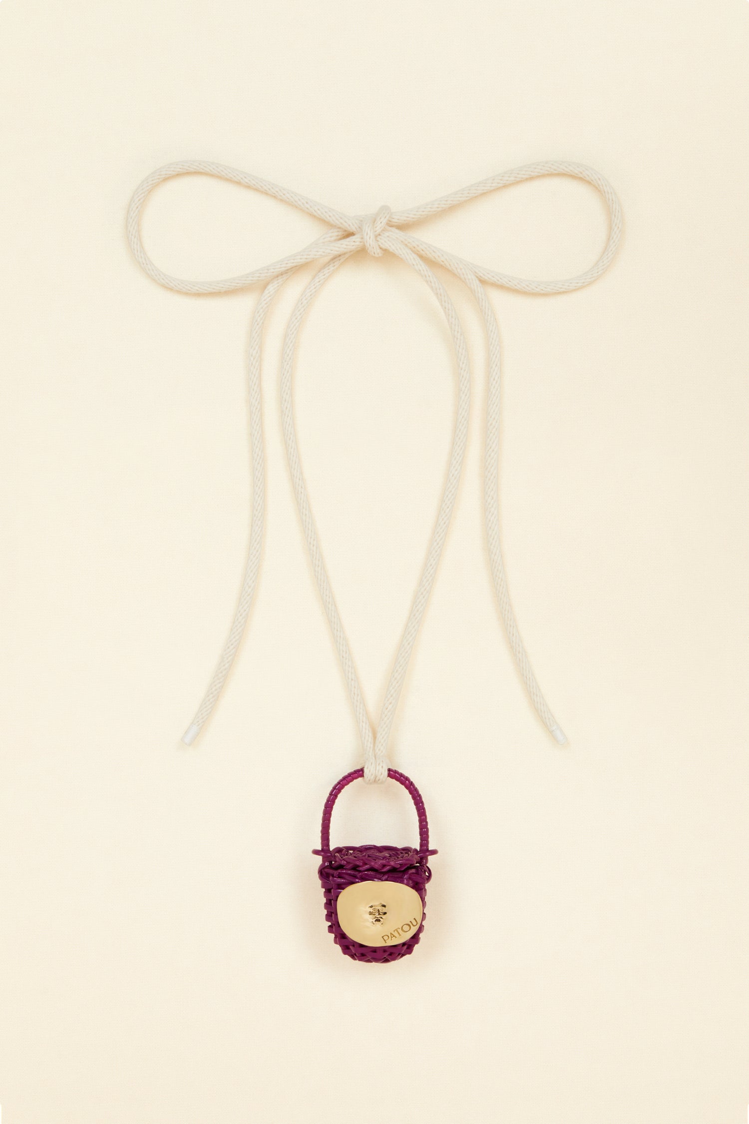 Patou - Bucket bag necklace in wicker - Anemone - A shiny amulet to carry your Patou everywhere with you. Ecru cord necklace with miniature wicker bucket bag pendant in Anemone purple. Top handle with a sliding lid. Gold-tone embellishment inspired by the Bocca della Verità"."