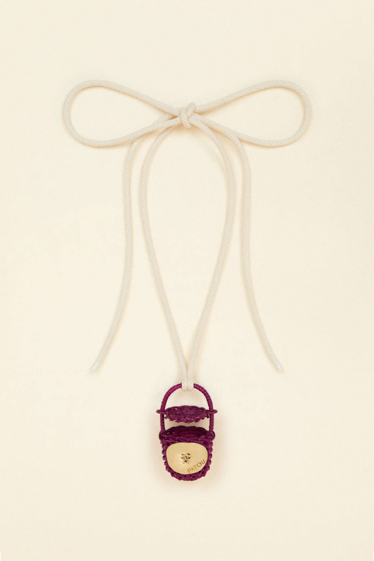 Patou - Bucket bag necklace in wicker - Anemone - A shiny amulet to carry your Patou everywhere with you. Ecru cord necklace with miniature wicker bucket bag pendant in Anemone purple. Top handle with a sliding lid. Gold-tone embellishment inspired by the Bocca della Verità"."