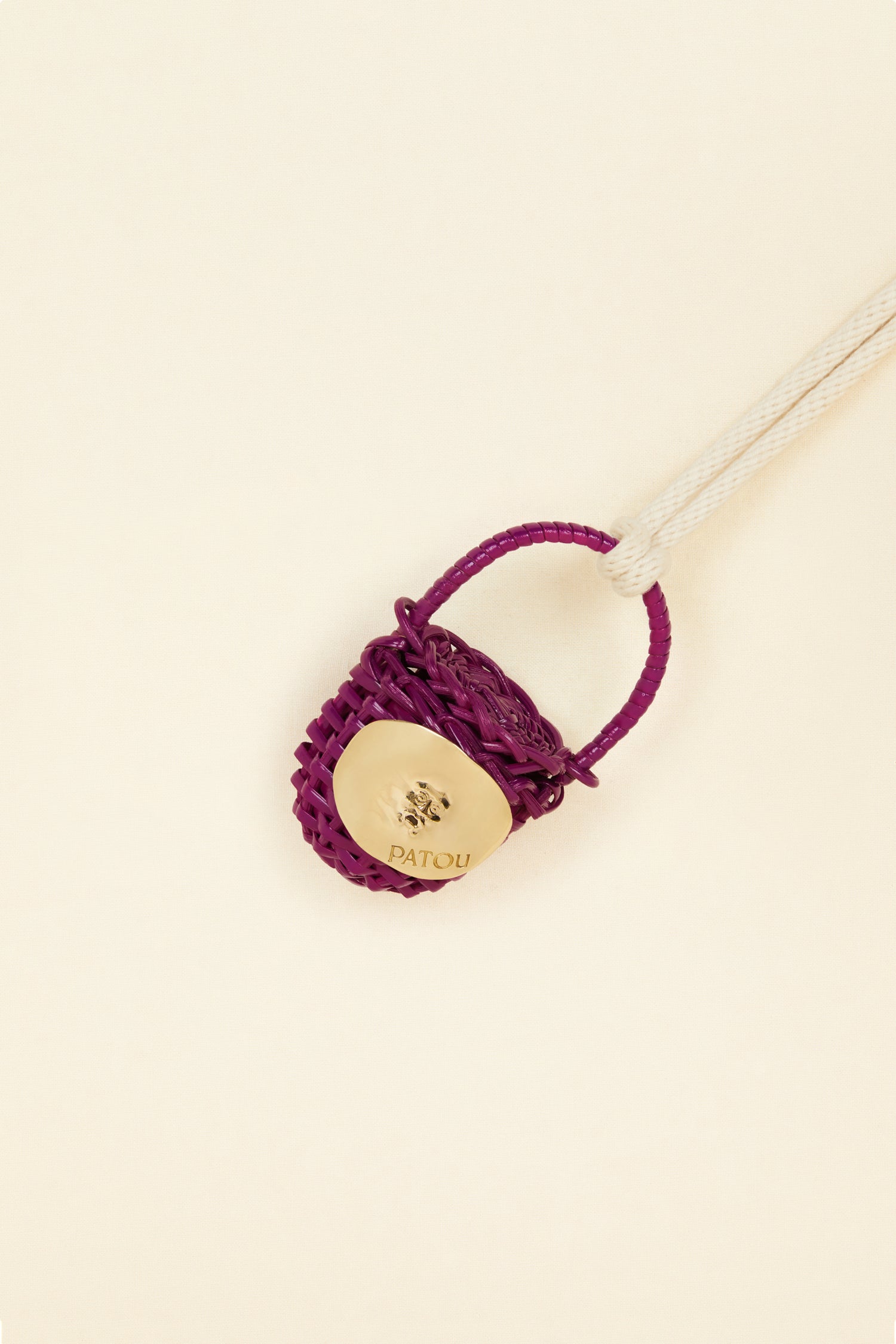 Patou - Bucket bag necklace in wicker - Anemone - A shiny amulet to carry your Patou everywhere with you. Ecru cord necklace with miniature wicker bucket bag pendant in Anemone purple. Top handle with a sliding lid. Gold-tone embellishment inspired by the Bocca della Verità"."