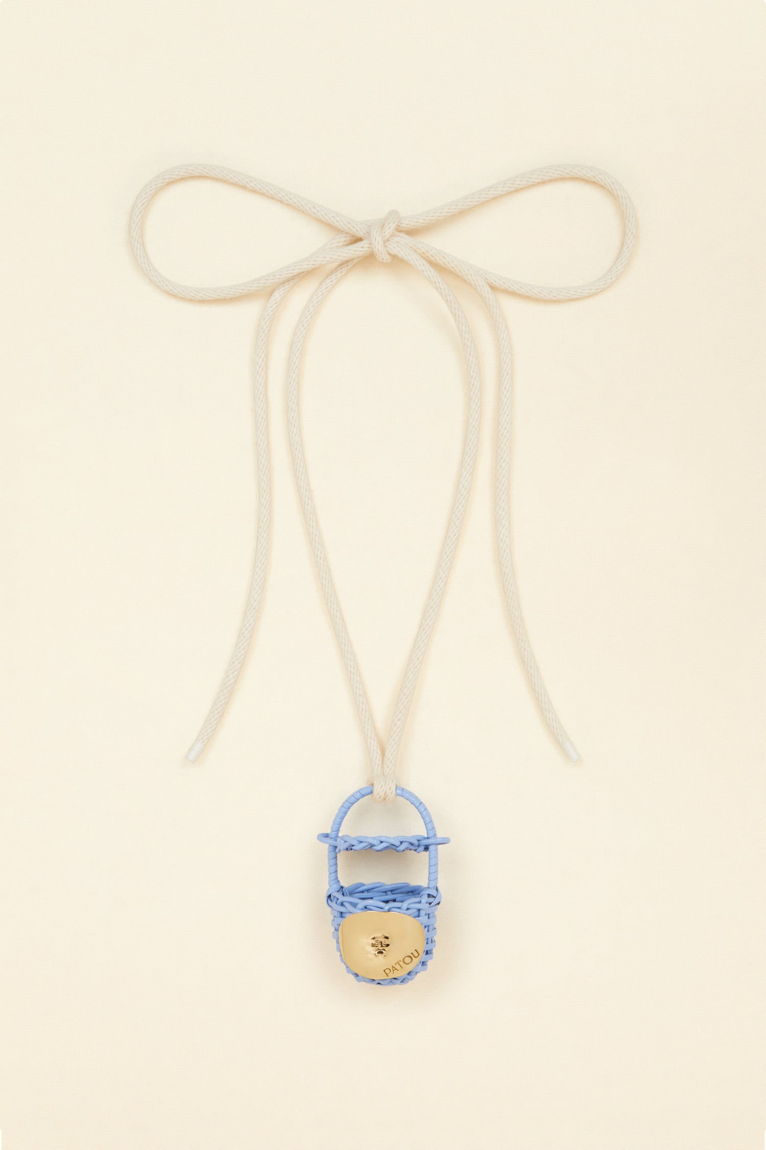 Patou - Bucket bag necklace in wicker - Aurora - A shiny amulet to carry your Patou everywhere with you. Ecru cord necklace with miniature wicker bucket bag pendant in Aurora light blue. Top handle with a sliding lid. Gold-tone embellishment inspired by the Bocca della Verità"."