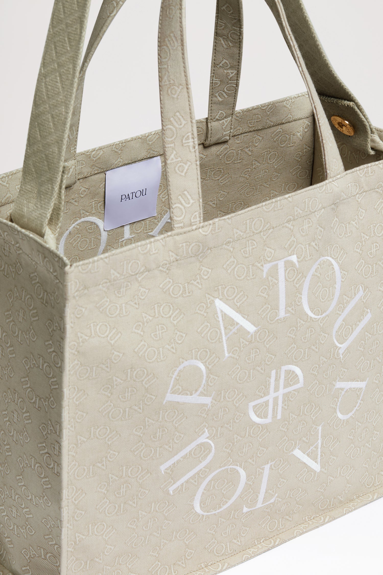 Patou - Patou canvas tote in organic cotton jacquard - Medallion - Carry your Patou everywhere with you. Organic cotton jacquard tote. Seasonal Medallion pattern featuring the Patou lettering logo and JP monogram all over. Patou lettering logo and JP monogram in white. Embossed shoulder strap with gold buttons. Two top handles. Can be carried by hand or on the shoulder.