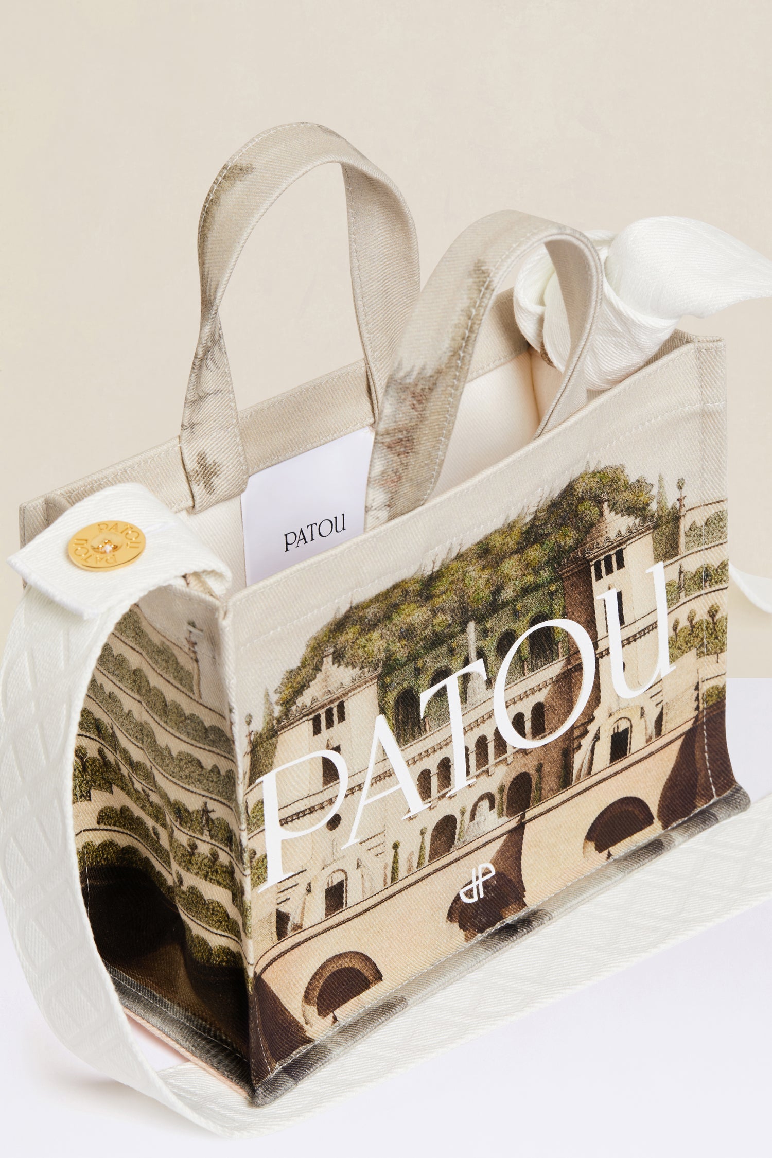 Patou - Small Patou canvas tote in printed organic cotton - Amour Island - A little Patou goes a long way.Organic cotton tote featuring Jean-Jacques Lequeu's “Amour Island” print. Patou lettering logo and JP monogram in white. White embossed shoulder strap with gold button on one side and adjustable knot on the other side. Two tone-on-tone top handles. Can be carried by hand or on the shoulder.