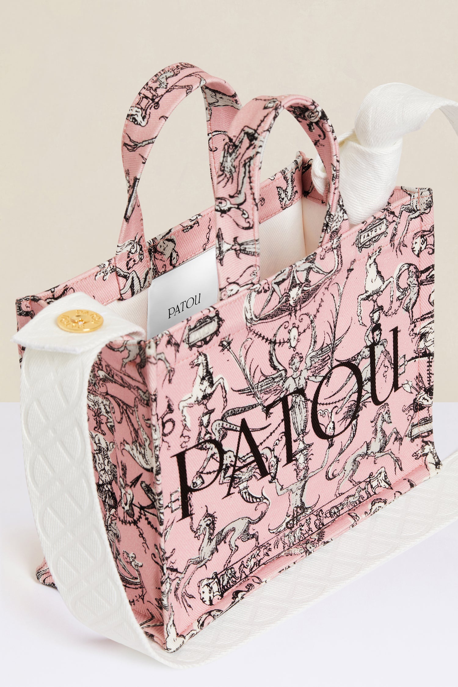 Patou - Small Patou canvas tote in printed organic cotton - Pink Fairy Tales - A tale of organic canvas and magical prints.Pink organic cotton tote. “Stories and Tales” seasonal print. Patou lettering logo and JP monogram in black. White embossed shoulder strap with gold button on one side and adjustable knot on the other side. Two tone-on-tone top handles. Can be carried by hand or on the shoulder.
