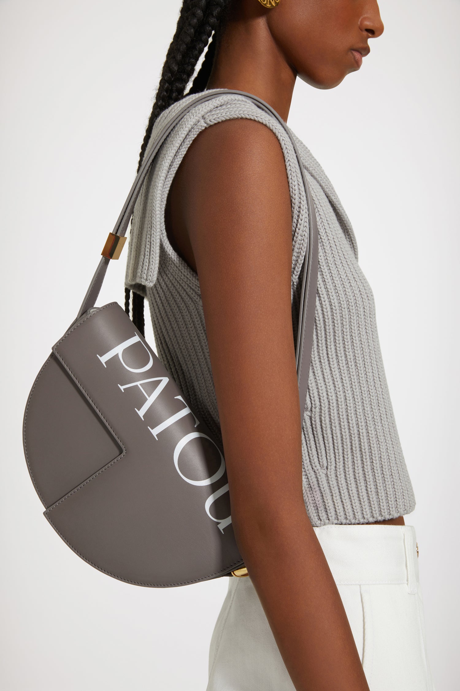 Patou - Le Patou logo - Storm Print - Le Patou a plus d'un tour dans son sac !Sac en cuir gris tempête. Maxi logo Patou. Réalisé en cuir de grande qualité provenant de stocks dormants issus des surplus de production. Édition limitée et numérotée disponible en 60 exemplaires. Forme demi-lune avec découpes géométriques inspirée du monogramme JP. Pièces en métal doré avec détail JP inspiré d'une broche des archives Jean Patou. Bandoulière ajustable permettant un porté épaule, en bandoulière ou à la main. Fermeture aimantée avec détail JP doré. Compartiments multiples à l'intérieur.Dimensions : 25 cm de longueur, 15 cm de hauteur et 6 cm de profondeurBandoulière ajustable en 3 longueurs : 47 cm (sur l'épaule), 36 cm (en bandoulière), 28 cm (porté à la main)