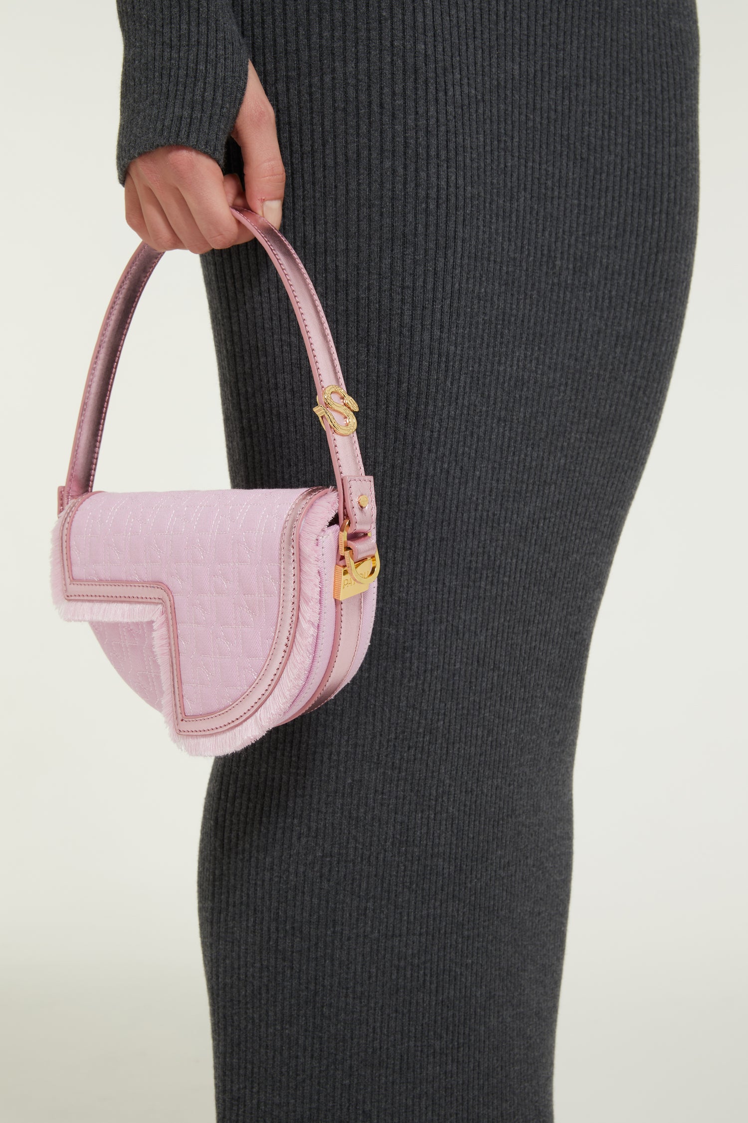 Patou - Le Petit Patou x Sita - Pink - Remixé et revisité, le Petit Patou plus culte que jamais !Sac en coton bio recyclé effet denim et cuir métallisé rose. Créé dans le cadre de la collaboration spéciale avec la DJ et styliste Sita Abellán. Réalisé en cuir de grande qualité provenant de stocks dormants issus des surplus de production. Forme demi-lune avec découpes géométriques inspirée du monogramme JP. Surpiqûres JP. Pièce métallique dorée gravée Patou sur le côté. Bordure soulignée de cuir avec détail de franges. Bandoulière en cuir amovible ornée d'un serpent, symbole signature de Sita, permettant au sac d'être porté sur l'épaule ou à la main. Peut être remplacée par une bandoulière en laiton (vendue séparément) ornée des lettres Patou et du serpent emblématique de Sita pour un porté épaule, en bandoulière ou à la taille afin de transformer Le Petit Patou en sac ceinture. Fermeture aimantée avec détail JP doré. Doublure éco-friendly. Dimensions : 20 cm de longueur, 13 cm de hauteur et 5 cm de profondeur.