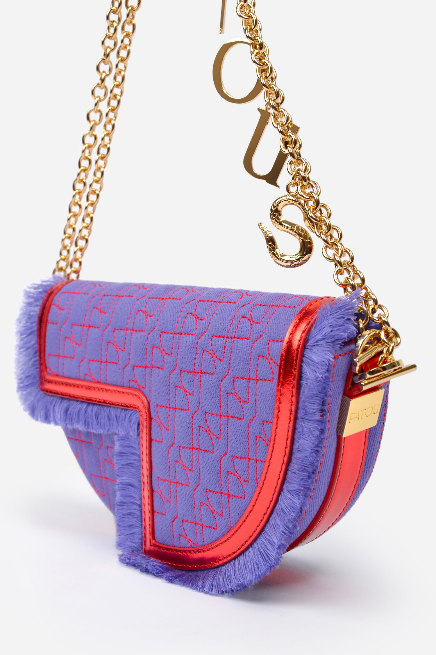 Patou - Le Petit Patou x Sita - Purple Blue Red - A high-octane remix on a Patou favouriteViolet denim-effect recycled organic cotton and red metallic leather handbag. Part of a special collaboration with DJ and designer Sita Abellán. Crafted using premium deadstock leather. Half-circle shape with geometric cut-outs inspired by the JP monogram. Allover JP quilting in red. Gold-tone hardware with Patou-engraved detail at the side. Leather outline with fringed edges. Removable leather strap adorned with Sita's signature snake that allows it to be worn on the shoulder or carried by hand. Might be replaced by a gold-tone brass chain strap (sold separately) adorned with Patou letter charms and Sita's snake symbol; the chain can be used as single or double length and worn on the shoulder, across the body or at the waist to turn Le Petit Patou into a belt bag. Magnetic closure with gold-tone JP detail. Internal compartment. Eco lining.Measures: 20cm (length), 13cm (height), 5cm (depth)