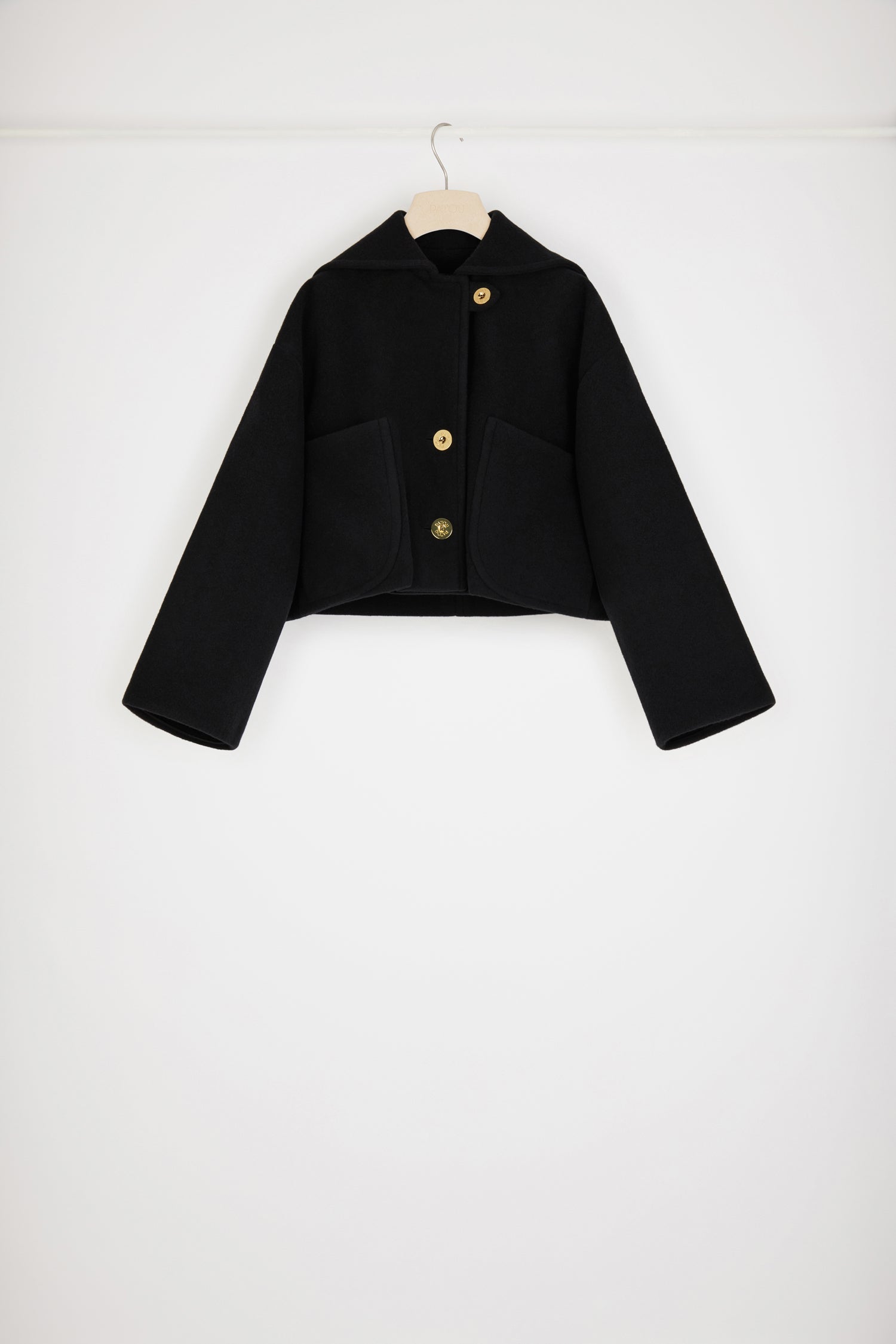 Patou - ダブルフェイスウール クロップコート - Black - シングルブレスト、ダブルフェイス:パトゥの勝利を約束するアウターのルール。ブラックのダブルフェイスウール製コート。丈の短いシルエット。シングルブレストデザイン、フロントでオフセンターボタン留め、トップにボタンループ。パトゥ刻印入りゴールドトーンボタン。セータースタイルのフラップカラー、バックにパトゥロゴ刺繍。オーバーサイズ パッチポケット。ルーズフィット(フィット感をお求めの場合はワンサイズ下をお選びください)。
