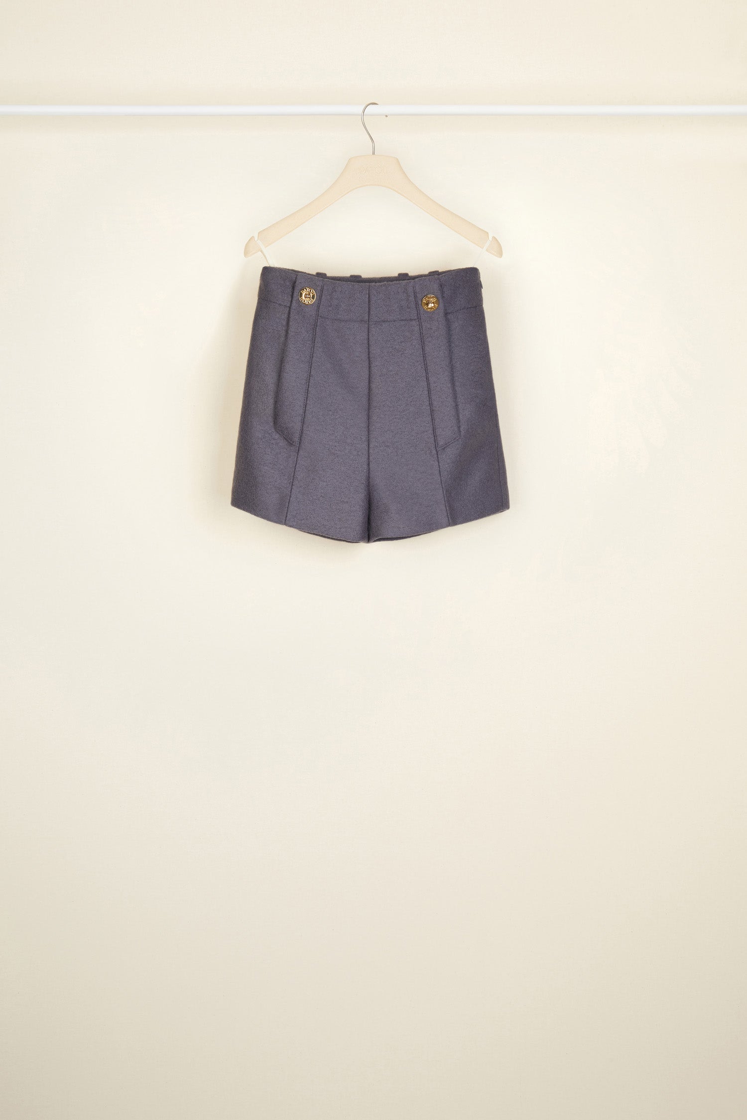 Patou - Hoch geschnittene Wollshorts - Storm - Kurze Shorts? Oui, aber à la Patou. Sturmgraue Shorts aus Walkwolle. Hoher Bund mit goldfarbenen Knöpfen mit Gravur am Taillenabschluss. Gürtelschlaufen, seitlicher Reißverschluss. Seitentaschen. Abnäher hinten.