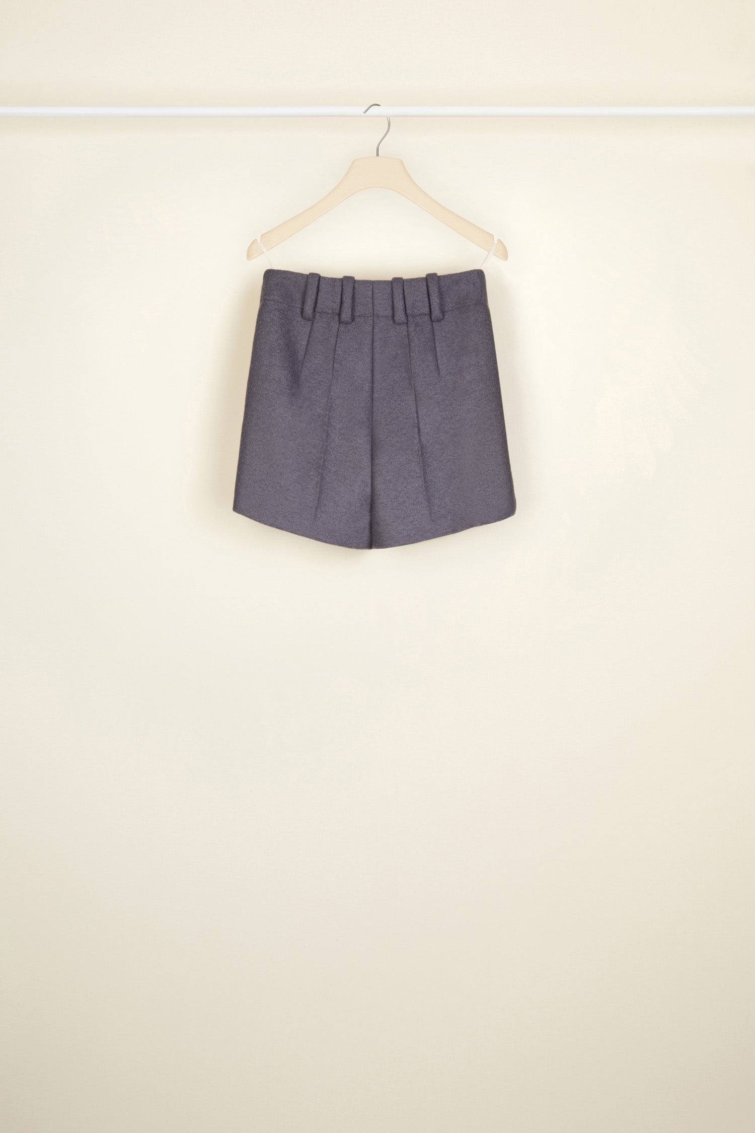 Patou - Hoch geschnittene Wollshorts - Storm - Kurze Shorts? Oui, aber à la Patou. Sturmgraue Shorts aus Walkwolle. Hoher Bund mit goldfarbenen Knöpfen mit Gravur am Taillenabschluss. Gürtelschlaufen, seitlicher Reißverschluss. Seitentaschen. Abnäher hinten.