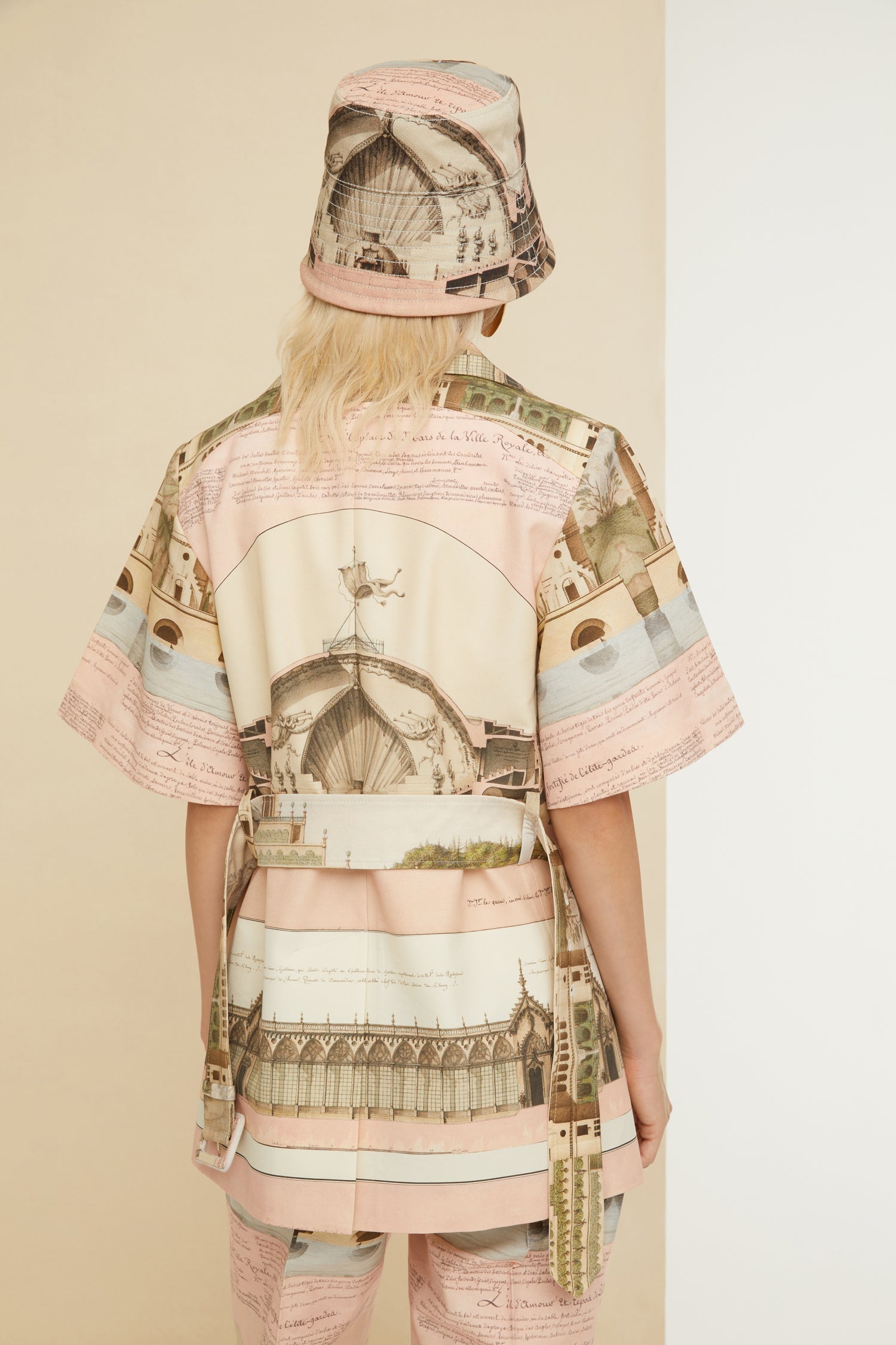 Patou - Belted short sleeve jacket in printed organic cotton and wool - Amour Island - Tailoring with a smile? Très Patou. Organic cotton and wool jacket featuring Jean-Jacques Lequeu's “Amour Island” print. Spread collar. Short sleeves with Patou label on the left cuff. Button fastening with fabric covered buttons. Curved seams at the bust with chest darts. Wide adjustable belt with fabric-covered. Seam pockets at the sides. Single vent at the back.