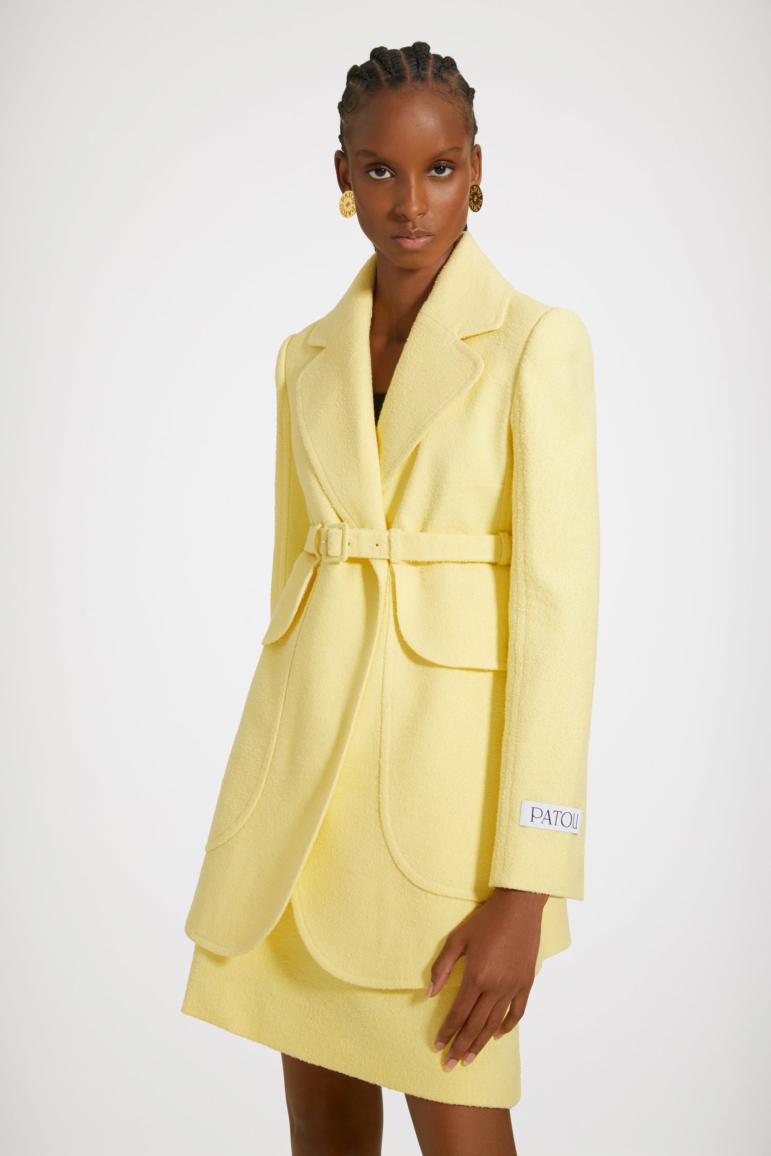 Patou - Longline belted jacket in cotton-blend tweed - Mimosa - Patou, a master tailor for the new generation. Mimosa yellow cotton-blend tweed jacket. Longline silhouette. Notch lapels. Concealed button fastening at the front with gold-tone Patou-engraved buttons. Signature curved seam at the back. Adjustable buckle belt that sits high at the waist. Maxi flap patch pockets at the front. Patou label on the left sleeve. Split cuffs. High back vent. Fully lined.Spring-Summer 2023 Show - Look #16