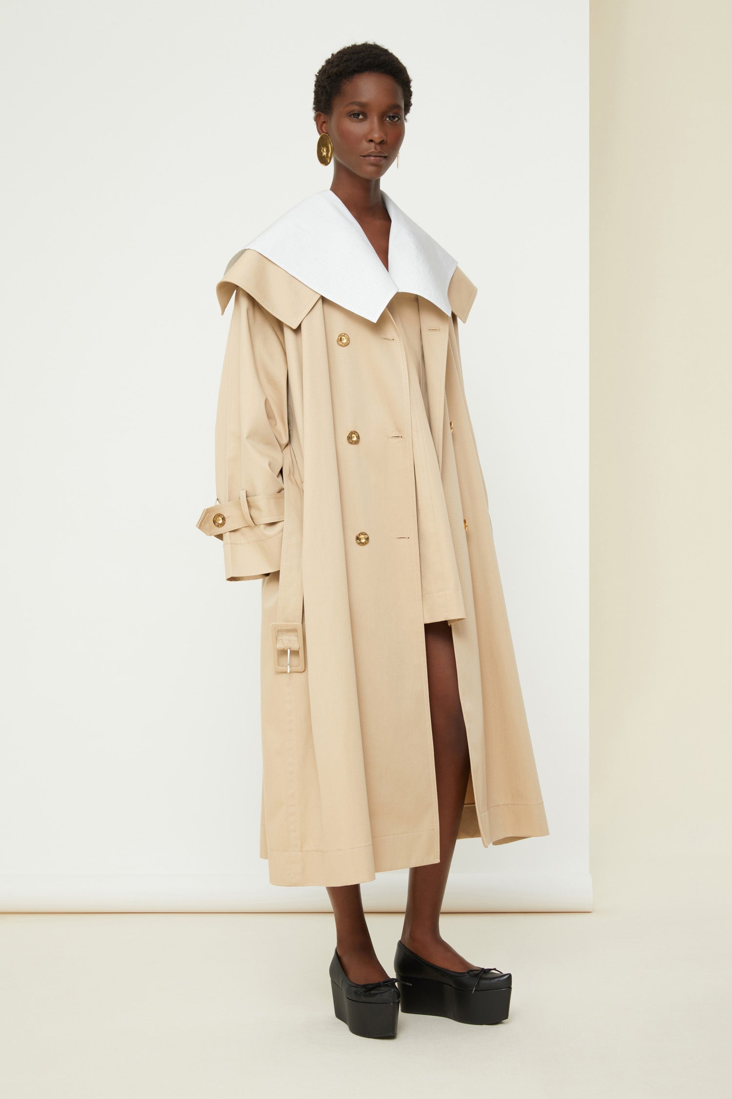 Patou - Charakteristischer Trenchcoat aus Bio-Baumwolle - Sand - Ein ausgestellter Trenchcoat mit französischem Flair. Charakteristischer Patou Trenchcoat aus sandbeiger Bio-Baumwoll-Gabardine. Doppelreihig mit leichter A-Linie. Übergroßer Kragen und Sturmklappe. Goldfarbene Knöpfe mit Patou Logo-Gravur. Abnehmbarer Taillengürtel. Bindebänder an den Manschetten mit schwarzem gestickten Patou Etikett. Zwei Seitentaschen. Vollständig gefüttert.