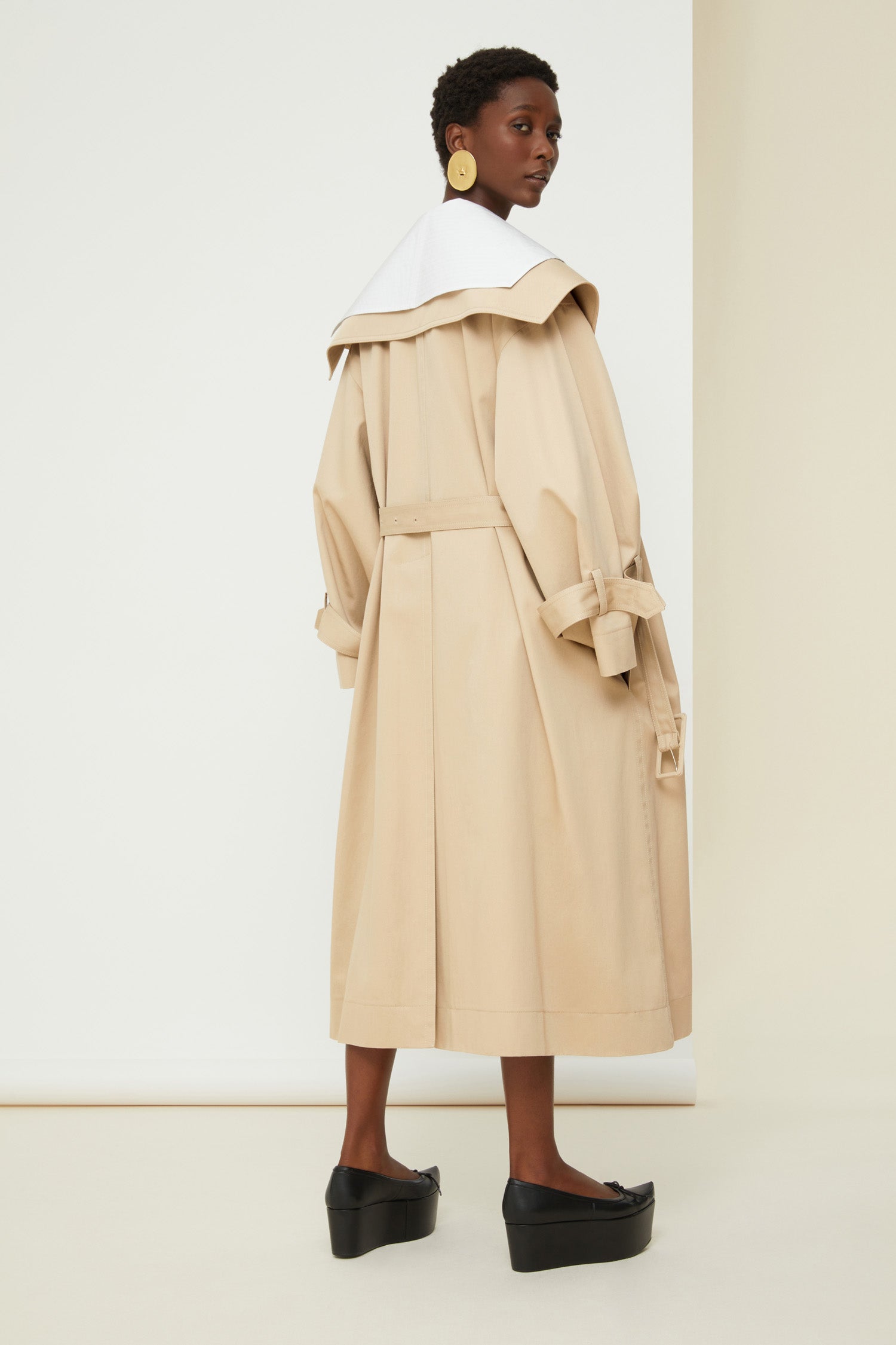 Patou - Charakteristischer Trenchcoat aus Bio-Baumwolle - Sand - Ein ausgestellter Trenchcoat mit französischem Flair. Charakteristischer Patou Trenchcoat aus sandbeiger Bio-Baumwoll-Gabardine. Doppelreihig mit leichter A-Linie. Übergroßer Kragen und Sturmklappe. Goldfarbene Knöpfe mit Patou Logo-Gravur. Abnehmbarer Taillengürtel. Bindebänder an den Manschetten mit schwarzem gestickten Patou Etikett. Zwei Seitentaschen. Vollständig gefüttert.