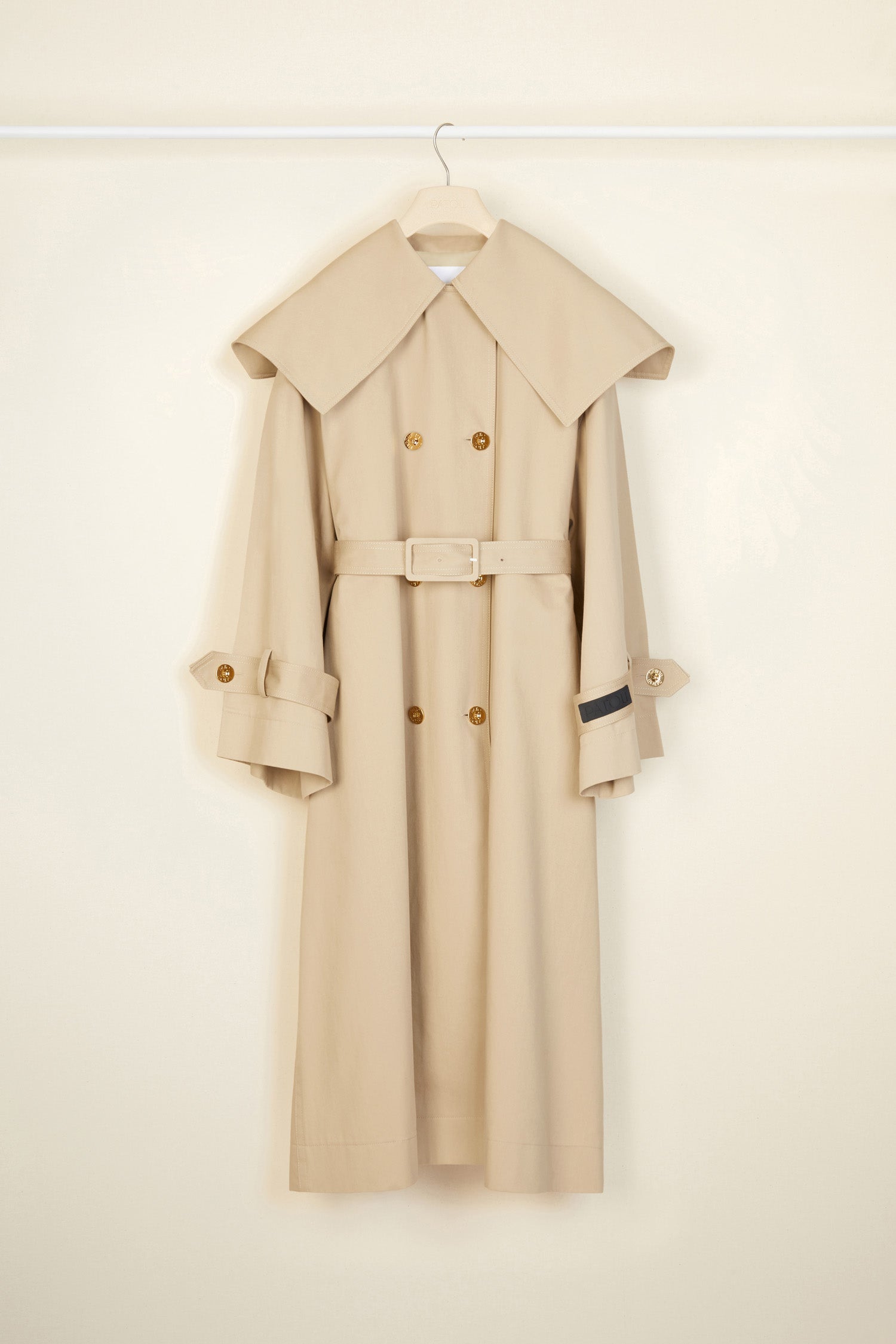 Patou - Charakteristischer Trenchcoat aus Bio-Baumwolle - Sand - Ein ausgestellter Trenchcoat mit französischem Flair. Charakteristischer Patou Trenchcoat aus sandbeiger Bio-Baumwoll-Gabardine. Doppelreihig mit leichter A-Linie. Übergroßer Kragen und Sturmklappe. Goldfarbene Knöpfe mit Patou Logo-Gravur. Abnehmbarer Taillengürtel. Bindebänder an den Manschetten mit schwarzem gestickten Patou Etikett. Zwei Seitentaschen. Vollständig gefüttert.