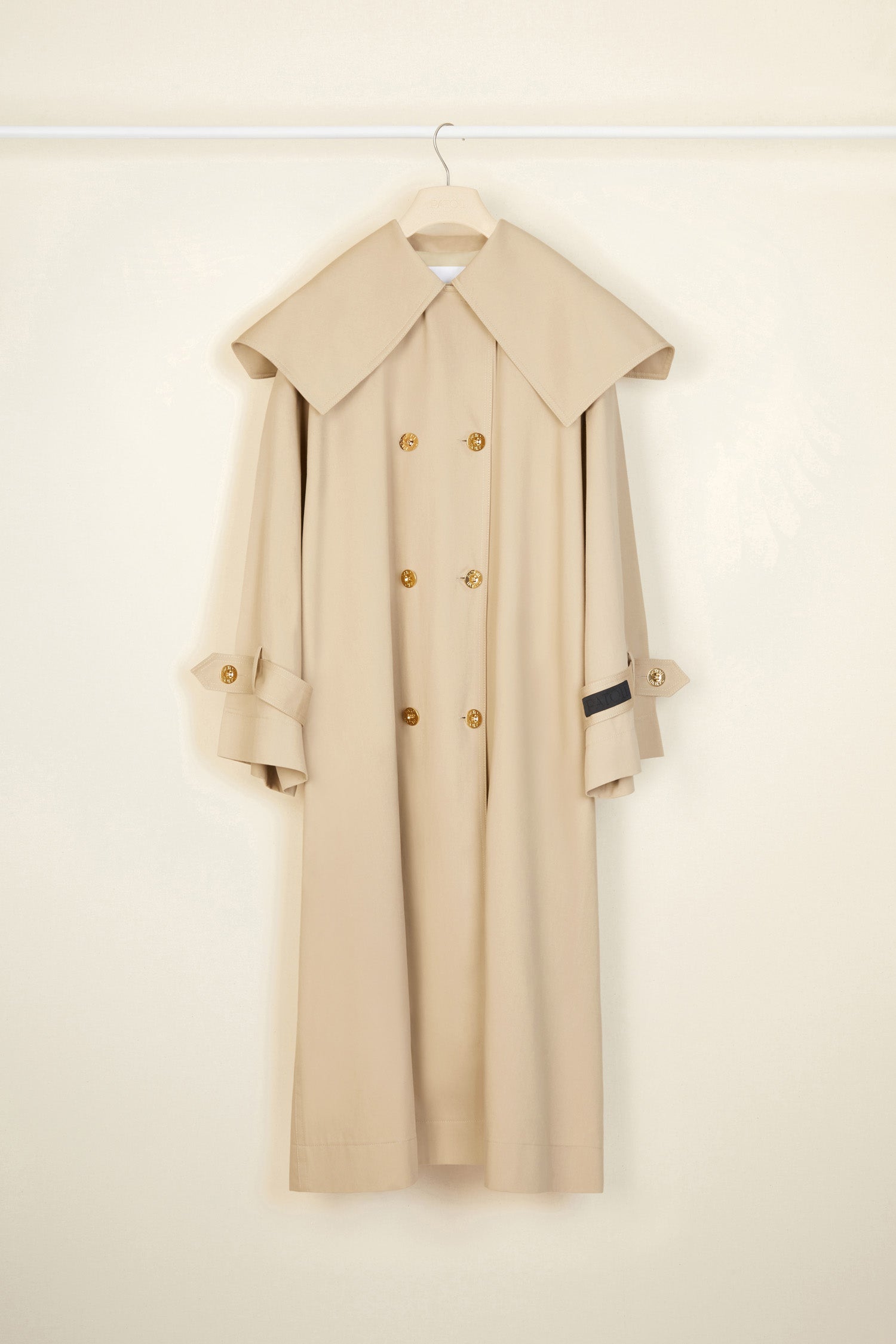Patou - Charakteristischer Trenchcoat aus Bio-Baumwolle - Sand - Ein ausgestellter Trenchcoat mit französischem Flair. Charakteristischer Patou Trenchcoat aus sandbeiger Bio-Baumwoll-Gabardine. Doppelreihig mit leichter A-Linie. Übergroßer Kragen und Sturmklappe. Goldfarbene Knöpfe mit Patou Logo-Gravur. Abnehmbarer Taillengürtel. Bindebänder an den Manschetten mit schwarzem gestickten Patou Etikett. Zwei Seitentaschen. Vollständig gefüttert.
