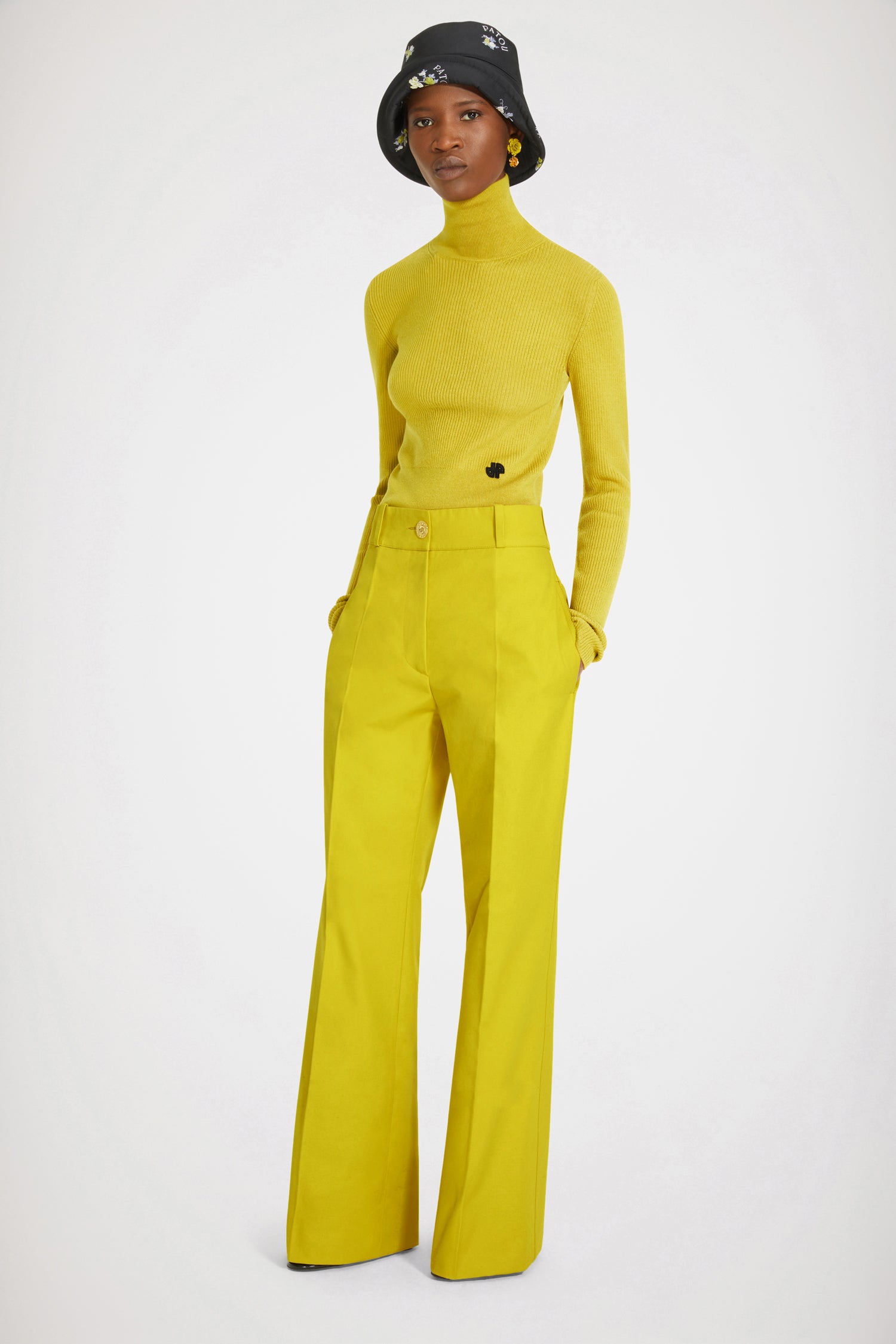 Patou - Flared trousers in organic cotton - Absinthe - Low rise, high craftsmanship: the perfect Patou trousers. Absinthe yellow organic cotton canvas trousers. Slightly flared straight leg with crease at the front and back. Low rise. Gold-tone Patou engraved button fastening at the front. Belt loops. Patou logo embroidered at the back. Pockets at the sides. Wide pockets at the back to complement the Eiffel tower construction.