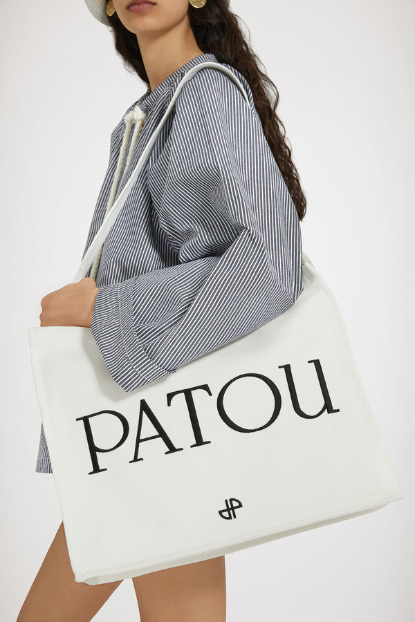 Patou - 오가닉 코튼 파투 캔버스 토트백 - Cream - 크림 컬러의 오가닉 코튼 소재. Patou 레터링 로고, 블랙 컬러의 JP 모노그램 장식. 한쪽 측면에 골드 버튼, 반대편에 사이즈 조절이 가능한 매듭 리본이 있는 엠보싱 처리된 화이트 숄더 스트랩. 두 개의 탑 핸들. 토트백 또는 숄더백으로 착용 가능.
