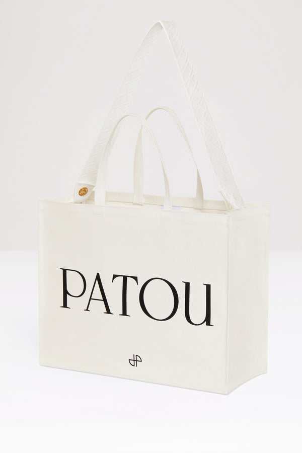 Patou - 오가닉 코튼 파투 캔버스 토트백 - Cream - 크림 컬러의 오가닉 코튼 소재. Patou 레터링 로고, 블랙 컬러의 JP 모노그램 장식. 한쪽 측면에 골드 버튼, 반대편에 사이즈 조절이 가능한 매듭 리본이 있는 엠보싱 처리된 화이트 숄더 스트랩. 두 개의 탑 핸들. 토트백 또는 숄더백으로 착용 가능.