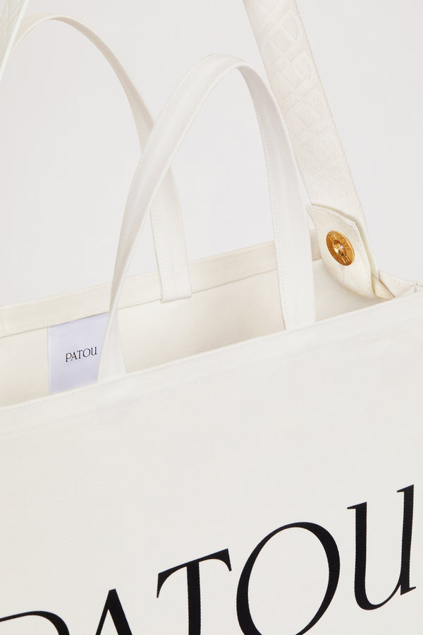 Patou - 오가닉 코튼 파투 캔버스 토트백 - Cream - 크림 컬러의 오가닉 코튼 소재. Patou 레터링 로고, 블랙 컬러의 JP 모노그램 장식. 한쪽 측면에 골드 버튼, 반대편에 사이즈 조절이 가능한 매듭 리본이 있는 엠보싱 처리된 화이트 숄더 스트랩. 두 개의 탑 핸들. 토트백 또는 숄더백으로 착용 가능.
