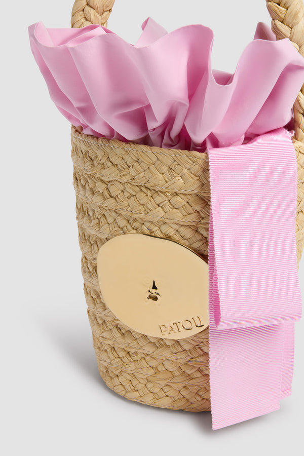 Patou - Sac Seau GG en Raphia - Primrose Pink - Sac seau naturel. Matière en raphia. Médaillon doré gravé Patou. Ruban rose.