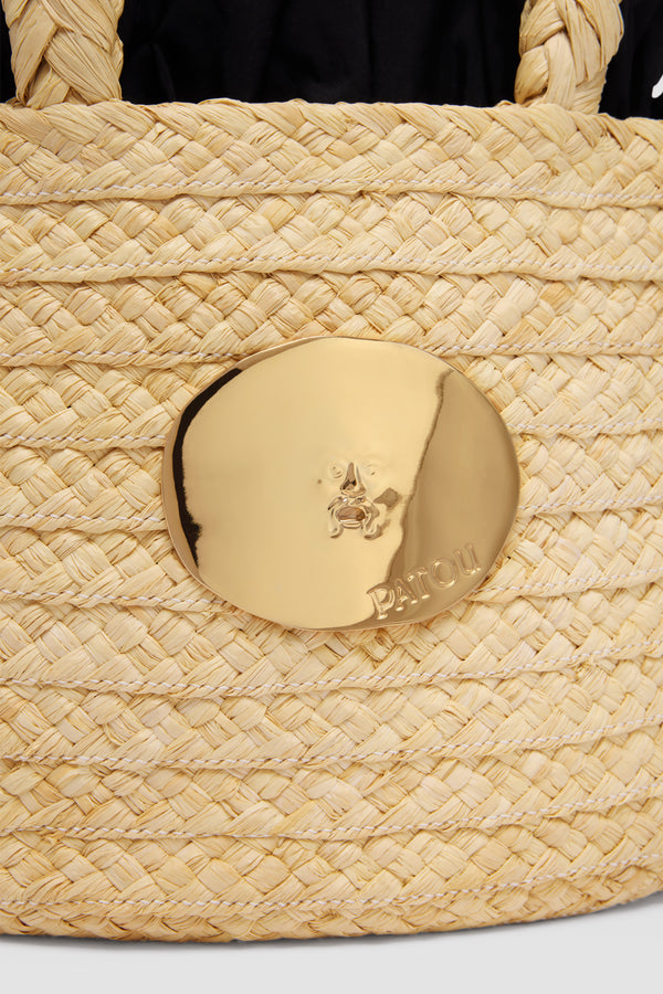 Patou - ラフィア アイコニック バスケット - Vanilla - バニラカラーの天然ラフィア製バスケット。編み込みのトップハンドル 2本。パトゥ ロゴのエングレービング入り、「真実の口」から着想を得たゴールドカラーの装飾。ブラックのファブリックライニング、ファイユフリル付き、グログランドローストリング付き。
