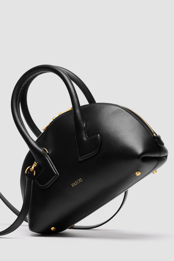 Patou - Borsa Le Patou Bowling in pelle - Black - Borsa in pelle liscia nera. Forma bowling. Doppio manico con dettagli geometrici. Tracolla rimovibile. Chiusura con zip oro a doppio cursore. Logo Patou oro sul davanti. Piedini in metallo oro.