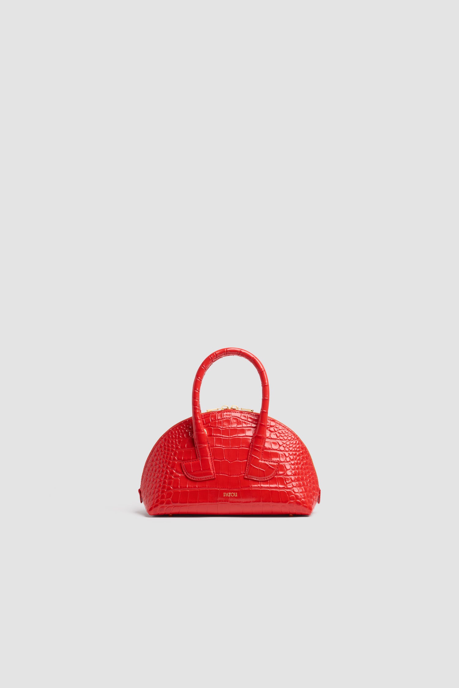 Patou - Le Patou Bowling bag in crocodile-embossed leather - Babylone Red - Babylone Red crocodile-embossed leather handbag. Bowling shape. Two top handles with geometric cut-out details. Removable shoulder strap. Two-way gold-tone top zip fastening. Gold-embossed Patou logo at the front. Gold-tone metal feet.