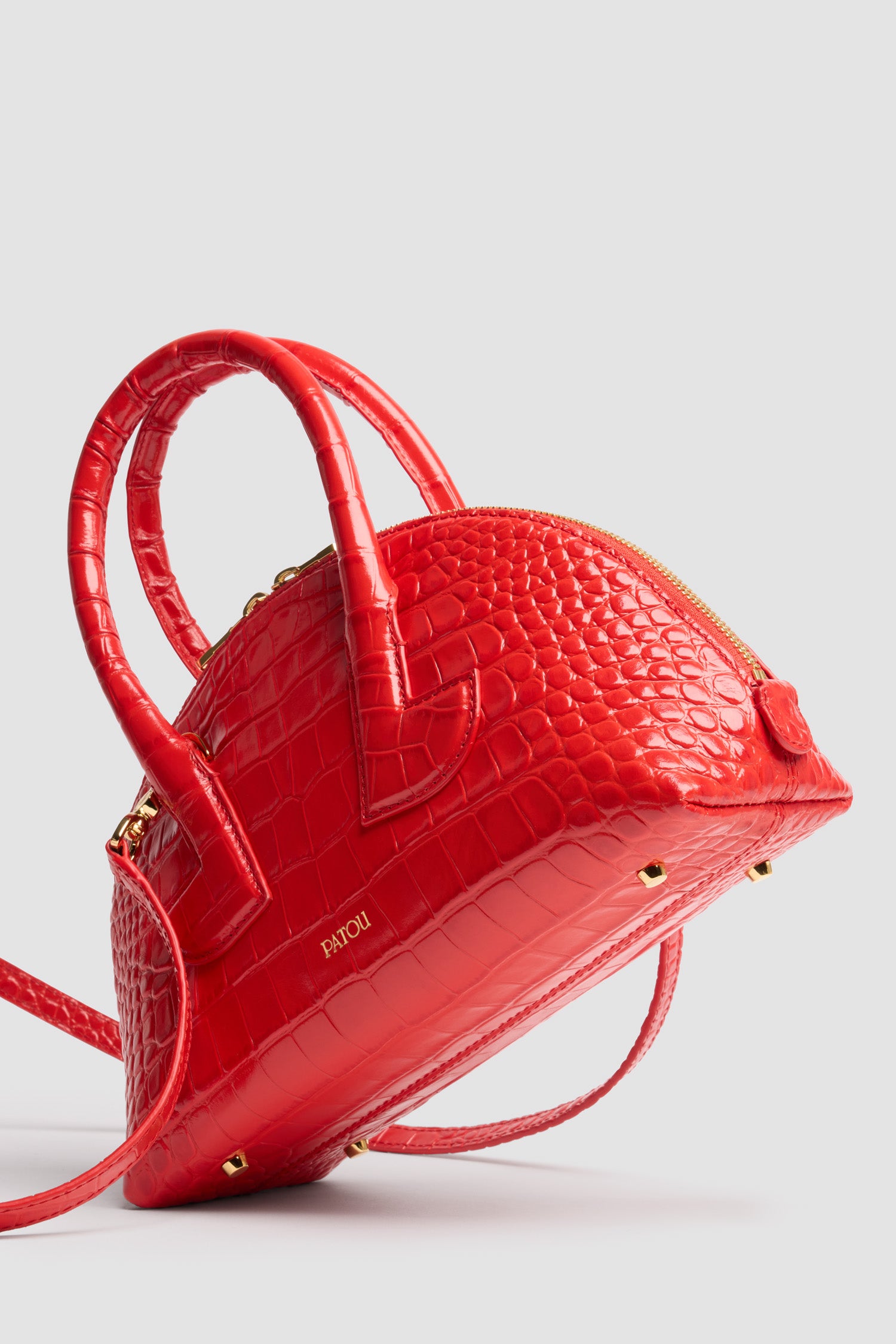 Patou - Le Patou Bowling bag in crocodile-embossed leather - Babylone Red - Babylone Red crocodile-embossed leather handbag. Bowling shape. Two top handles with geometric cut-out details. Removable shoulder strap. Two-way gold-tone top zip fastening. Gold-embossed Patou logo at the front. Gold-tone metal feet.