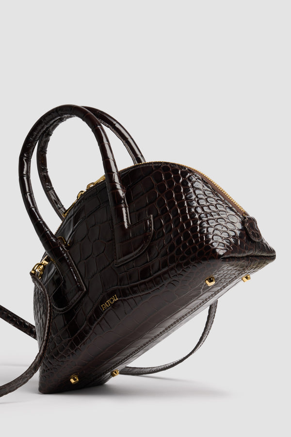 Patou - Borsa Le Patou Bowling in pelle di coccodrillo goffrata - Smoked Ebony - Borsa in pelle di coccodrillo goffrata Smoked Ebony. Forma bowling. Doppio manico con dettagli geometrici. Tracolla rimovibile. Chiusura con zip oro a doppio cursore. Logo Patou oro goffrato sul davanti. Piedini in metallo oro.