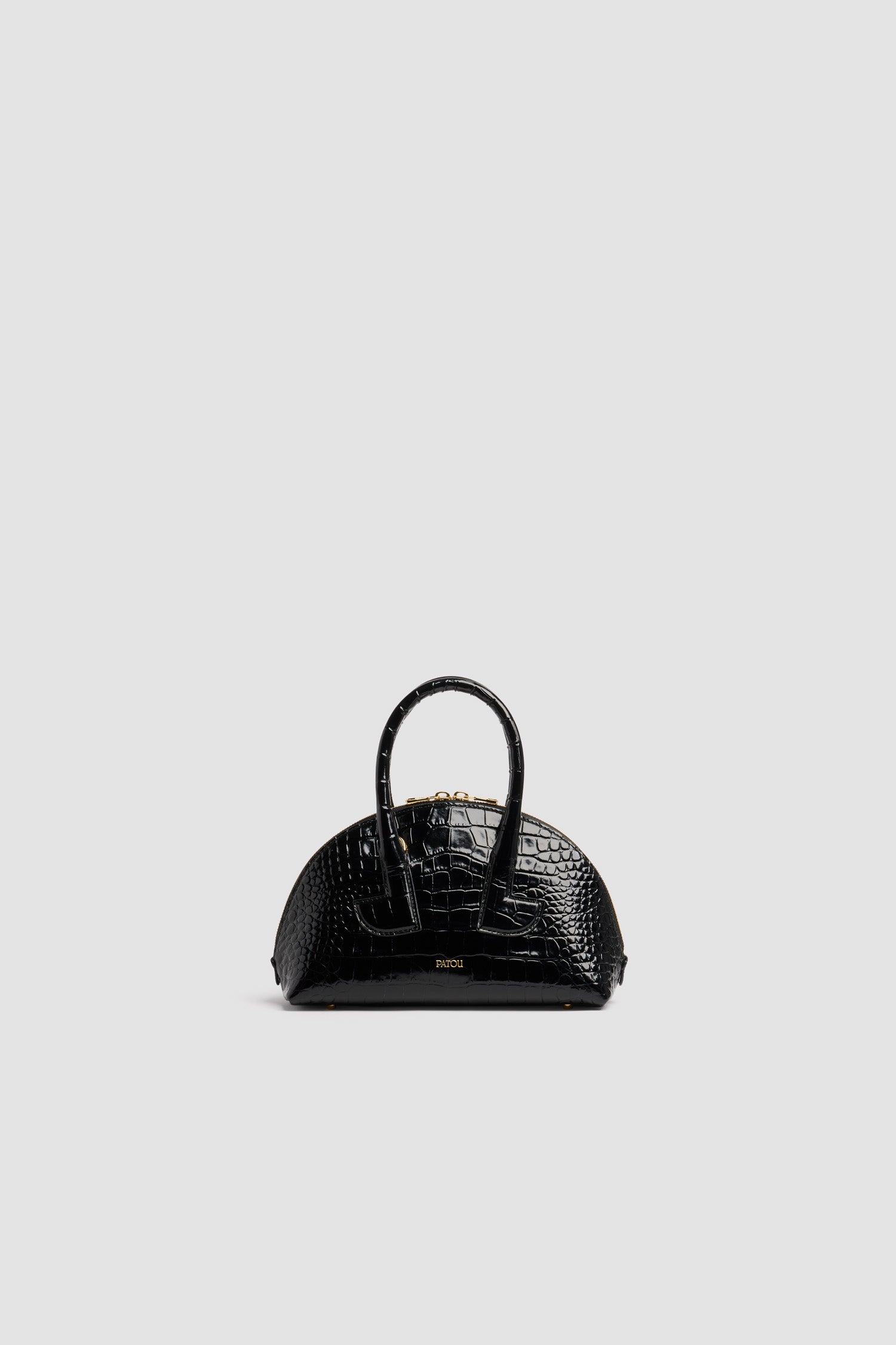 Patou - Le Patou Bowling bag in crocodile-embossed leather - Black - Black crocodile-embossed leather handbag. Bowling shape. Two top handles with geometric cut-out details. Removable shoulder strap. Two-way gold-tone top zip fastening. Gold-embossed Patou logo at the front. Gold-tone metal feet.
