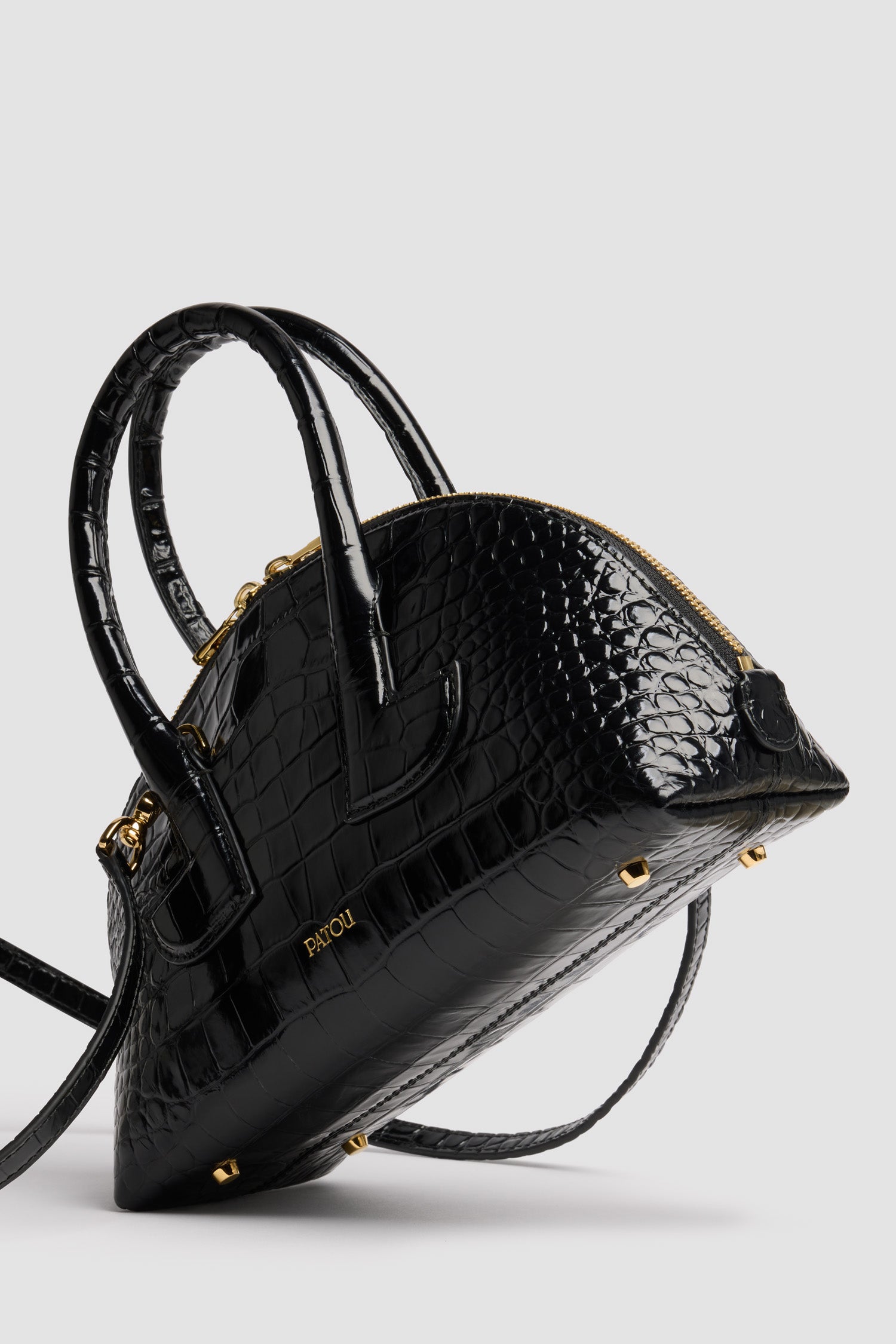 Patou - Le Patou Bowling bag in crocodile-embossed leather - Black - Black crocodile-embossed leather handbag. Bowling shape. Two top handles with geometric cut-out details. Removable shoulder strap. Two-way gold-tone top zip fastening. Gold-embossed Patou logo at the front. Gold-tone metal feet.