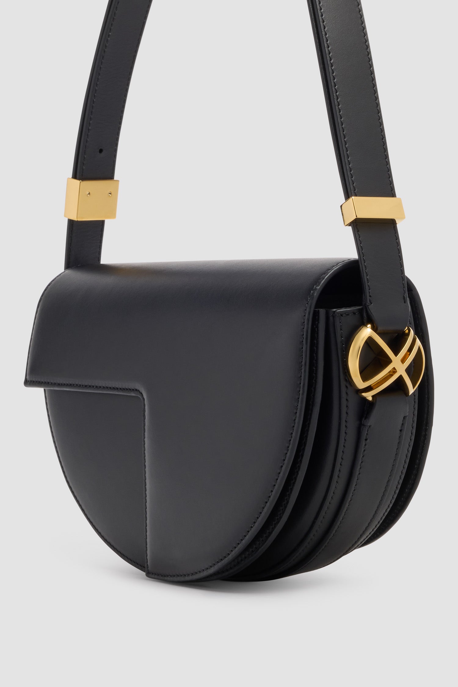 Patou - レザー製 Le Patou バッグ - Black - ブラックのスムースレザー製ハンドバッグ。JPモノグラムにインスピレーションを得た幾何学的なカットアウトをあしらった半円形のフォルム。サイドにゴールドトーンのメタルパーツとJPモノグラム ディテール。調整可能なストラップで、ショルダーバッグ、クロスボディバッグ、ハンドバッグとしてお使いいただけます。ゴールドトーンのJPディテールをあしらったマグネットクロージャー。内部に複数のコンパートメント。長さ: 長さ: 25cm、高さ: 15cm、幅: 6cmストラップの長さは3段階で調節可能：47 cm (ショルダー)、36 cm (クロスボディ)、28 cm (ハンド)