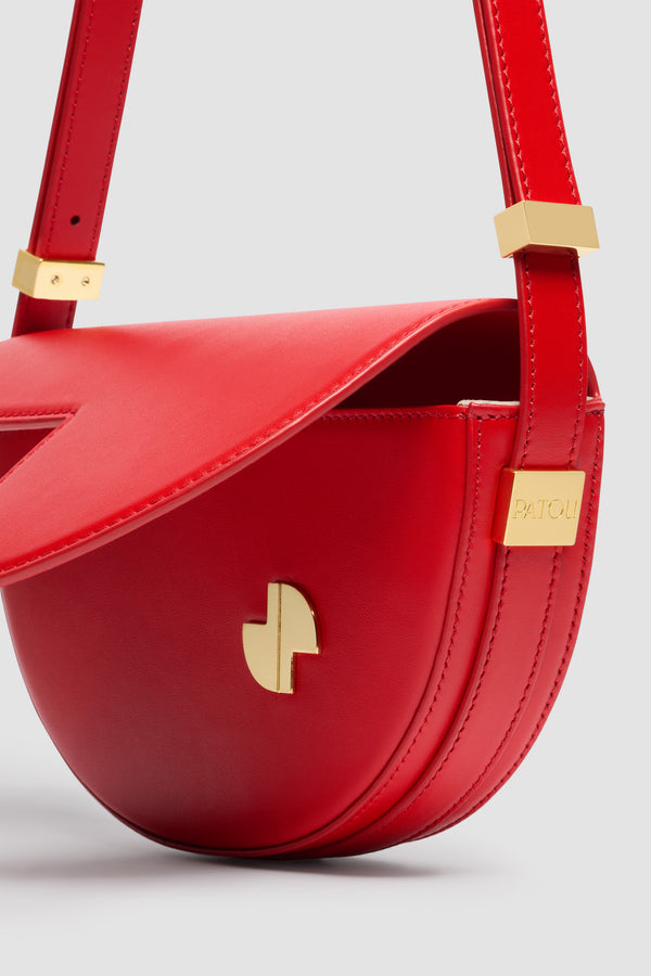 Patou - Le Petit Patou bag in leather - Lipstick Red - Lipstick Red smooth leather handbag. Half-circle shape with geometric cut-outs inspired by the JP monogram. Gold-tone hardware with Patou logo-engraved detail at the side. Adjustable strap that allows it to be worn on the shoulder, across the body or carried by hand. Magnetic closure with gold-tone JP detail. Internal compartment.Measures: 20 cm (length), 13 cm (height), 5 cm (depth)