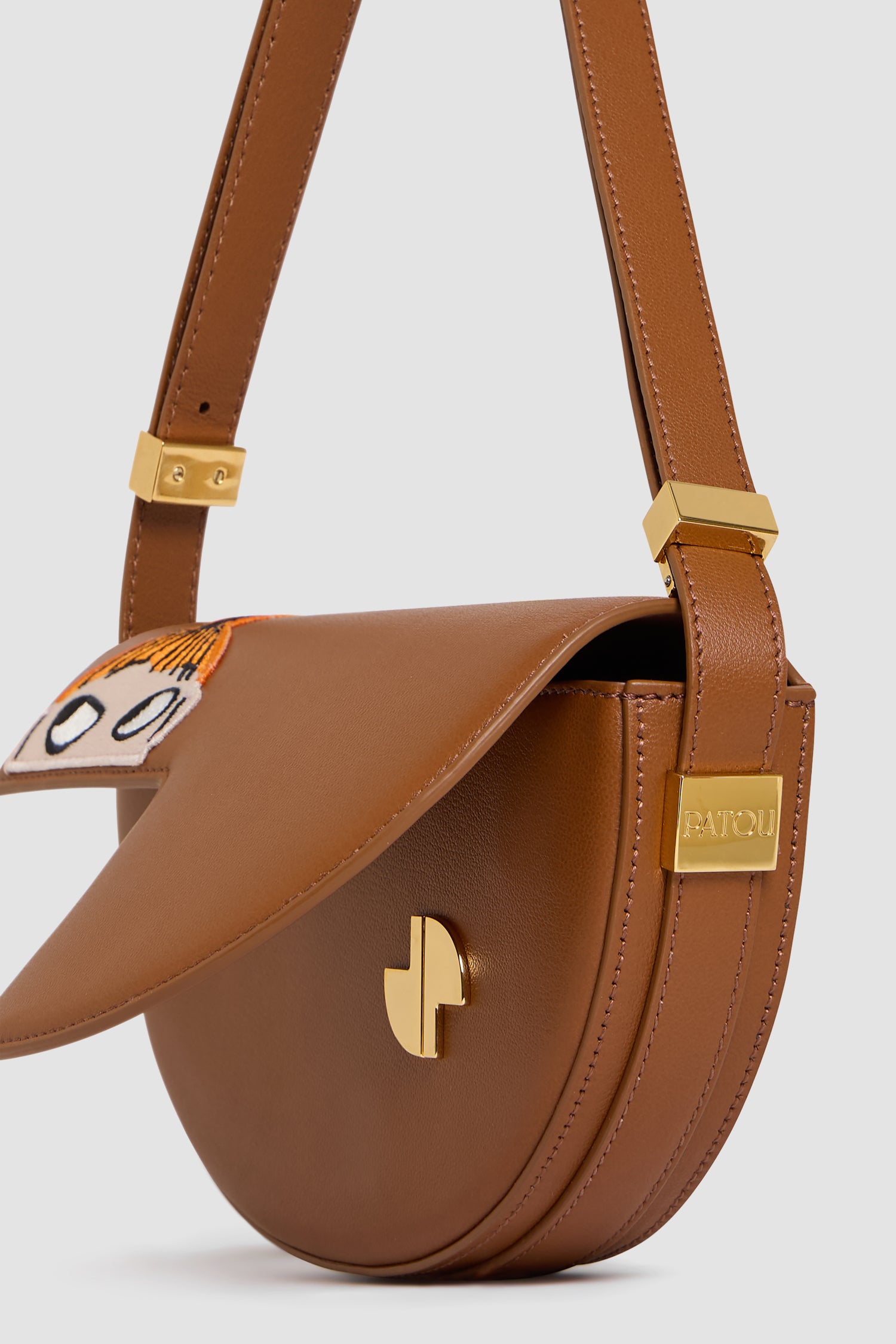 Patou - Patou x Moomin リトルミイ プチパトゥ レザーバッグ - Little My Cinnamon - Patou x Moomin が贈る、心温まるホリデーコレクション。アイコニックなプチパトゥバッグは、JPモノグラムからインスパイアされた幾何学的なカットと特徴的な半月型が魅力。上質なカーフレザーを使用し、リトルミイのディテールがあなたの装いに個性を添えます。調節可能なストラップでショルダー、クロスボディ、ハンドバッグとしてお楽しみいただけます。長さ: 20 cm 高さ:13 cm 幅：5 cm