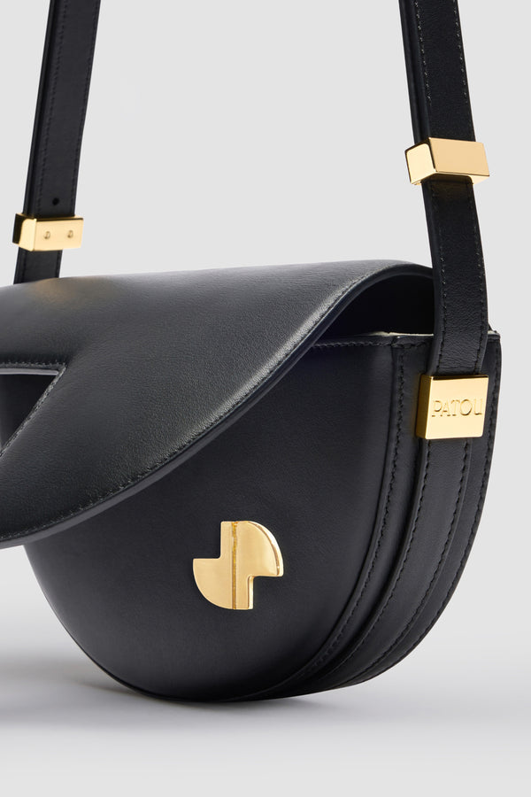 Patou - Le Petit Patou - Black - Sac en cuir noir. Forme demi-lune avec découpes géométriques inspirée du monogramme JP. Pièce métallique gravée Patou sur le côté. Bandoulière ajustable permettant un porté épaule, en bandoulière ou à la main. Fermeture aimantée avec détail JP doré. Doublure éco-friendly.Dimensions : 20 cm de longueur, 13 cm de hauteur et 5 cm de profondeur