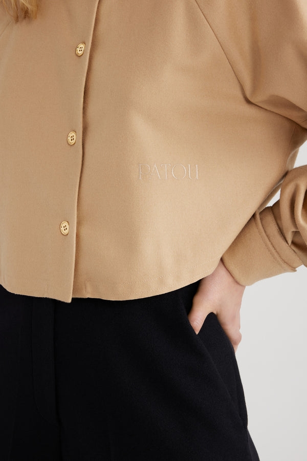Patou - サステナブル ウールブレンド クロップド シャツ - Gray Sand - グレーサンドのサステナブル ウール混フランネルシャツ。クロップド丈。シャツカラー。ゴールドトーンのJP刻印入りボタン。フロントにパトゥの刺繍。ラグランスリーブ。袖口にボタン付き。