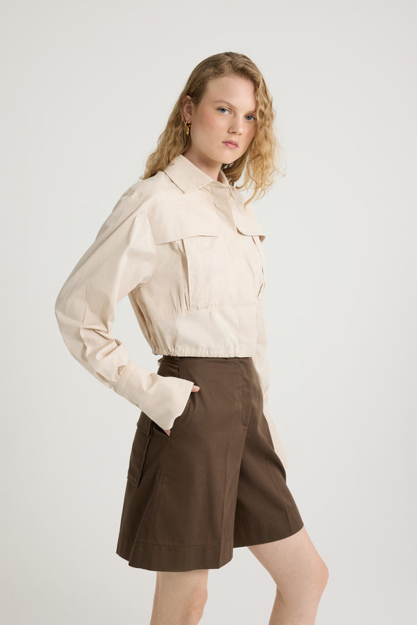 Patou - Camicia safari corta in popeline di cotone bio - Tapioca - Camicia in popeline di cotone bio beige tapioca. Modello corto. Colletto classico. Abbottonatura nascosta. Tasche a toppa alte sul petto. Maniche allungate con polsini abbottonati. Monogramma JP ricamato sulla manica sinistra. Piega sul retro. Vita con coulisse con allacciatura sul retro.