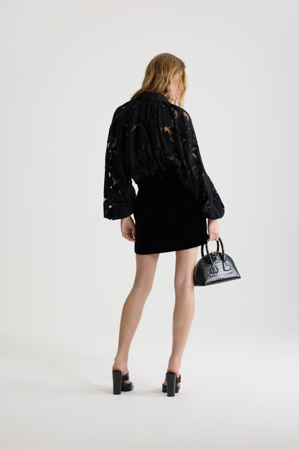 Patou - Blouse bouffante en dentelle de coton bio mélangé - Black - Blouse en dentelle de coton bio mélangé noire. Silhouette volumineuse. Modèle légèrement court. Col chemise classique. Fermeture par bouton dissimulé à l’avant. Manches ballon avec poignets élastiques. Ourlet bouffant.