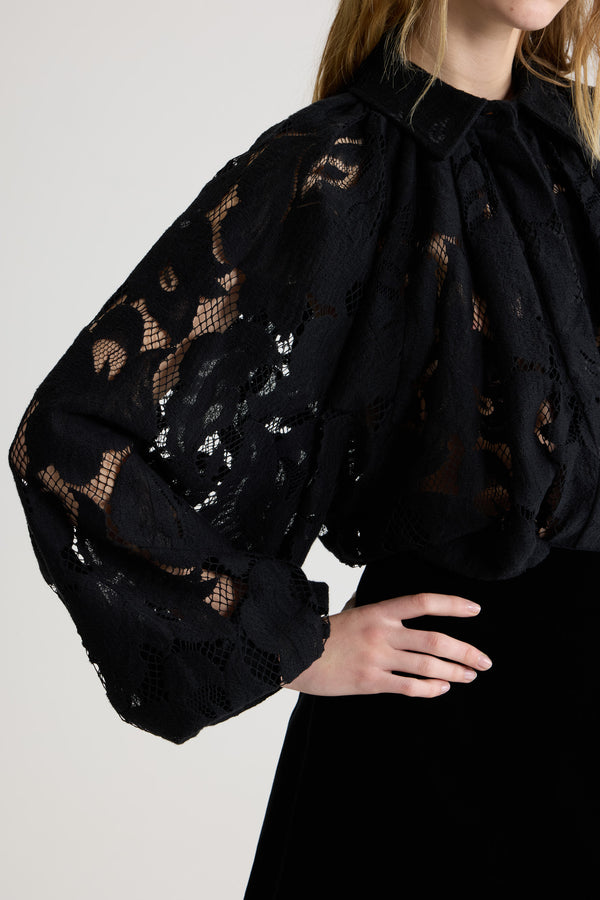 Patou - Blouse bouffante en dentelle de coton bio mélangé - Black - Blouse en dentelle de coton bio mélangé noire. Silhouette volumineuse. Modèle légèrement court. Col chemise classique. Fermeture par bouton dissimulé à l’avant. Manches ballon avec poignets élastiques. Ourlet bouffant.