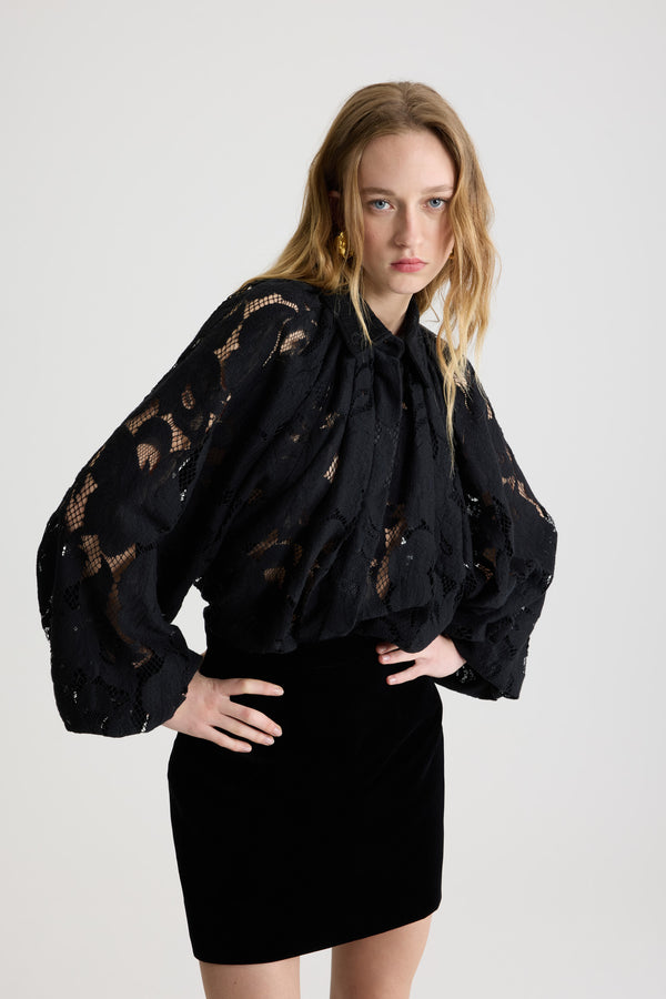 Patou - Blouse bouffante en dentelle de coton bio mélangé - Black - Blouse en dentelle de coton bio mélangé noire. Silhouette volumineuse. Modèle légèrement court. Col chemise classique. Fermeture par bouton dissimulé à l’avant. Manches ballon avec poignets élastiques. Ourlet bouffant.