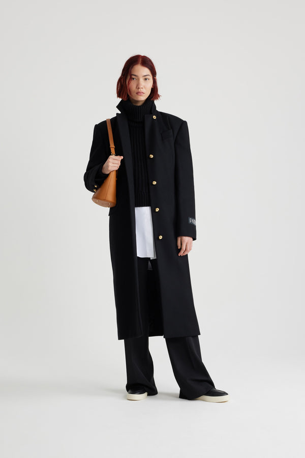 Patou - サステナブルウール＆カシミアブレンド テーラードコート - Black - ブラックのサステナブル ウール＆カシミア混紡コート。ロング丈。ストレートシルエット。立体的なショルダー。ハイカラー。コントラストカラーの裏地。ゴールドトーンのJP刻印と半球のJPボタン。片胸ポケット、フラップポケット2つ。ウエストに調節可能なバックルベルト。袖口にボタン付き。左袖にパトゥラベル。バックにハイベント。裏地付き。存在感のあるショルダーデザイン。