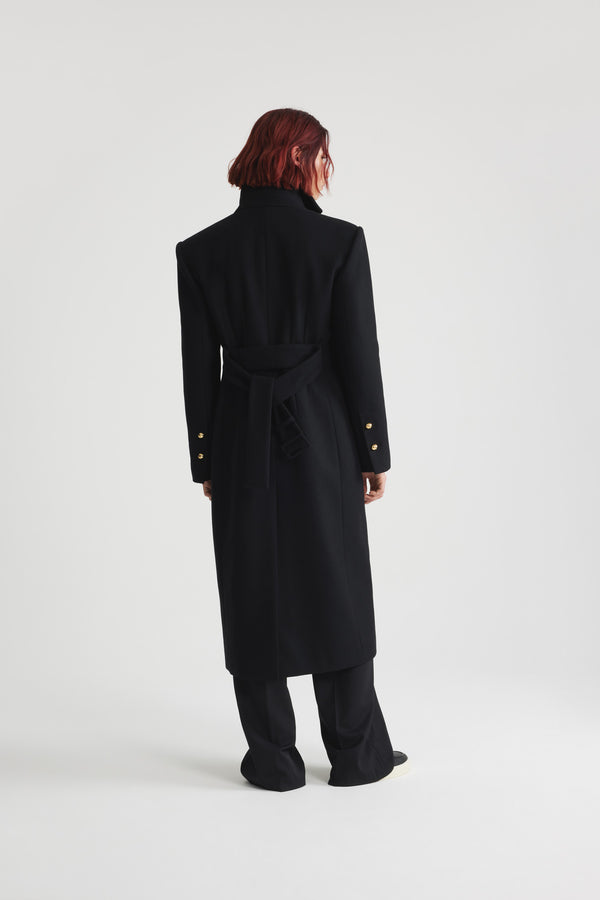 Patou - サステナブルウール＆カシミアブレンド テーラードコート - Black - ブラックのサステナブル ウール＆カシミア混紡コート。ロング丈。ストレートシルエット。立体的なショルダー。ハイカラー。コントラストカラーの裏地。ゴールドトーンのJP刻印と半球のJPボタン。片胸ポケット、フラップポケット2つ。ウエストに調節可能なバックルベルト。袖口にボタン付き。左袖にパトゥラベル。バックにハイベント。裏地付き。存在感のあるショルダーデザイン。