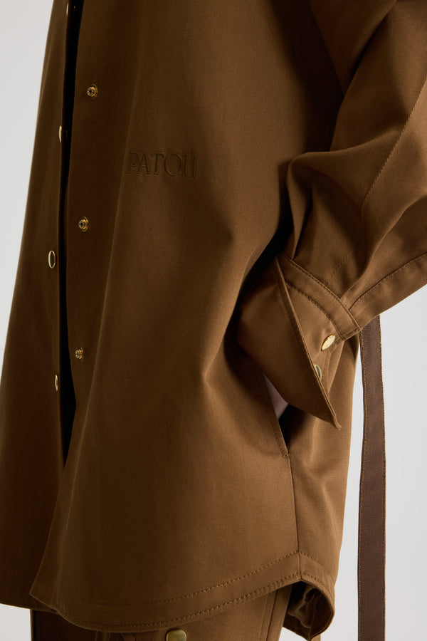 Patou - 오가닉 코튼 개버딘 소재 미니 셔츠 드레스 - Nutmeg - 너트메그 라이트 브라운 컬러의 오가닉 코튼 개버딘 드레스. 짧은 길이. 스트레이트 실루엣. 셔츠 칼라. 골드톤 JP 인그레이빙 버튼. 숄더 탭. 볼륨 래글런 슬리브. 버튼 디테일의 커프스. 탈착 가능한 허리 부분의 셀프 타이 벨트. 앞면의 JP 모노그램 및 파투 로고 자수 장식.