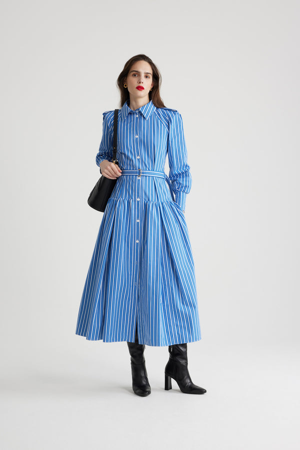 Patou - Robe chemise longue en coton imprimé éco-responsable - Victoria Blue Stripes - Robe en popeline de coton éco-responsable bleu Victoria. Motif rayures. Modèle long. Jupe volumineuse à étages. Col de chemise. Boutons en nacre gravés JP. Pattes d&#39;épaules. Manches raglan. Poignets boutonnés. Ceinture amovible à la taille avec boucle dorée.