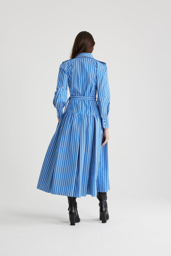 Patou - Robe chemise longue en coton imprimé éco-responsable - Victoria Blue Stripes - Robe en popeline de coton éco-responsable bleu Victoria. Motif rayures. Modèle long. Jupe volumineuse à étages. Col de chemise. Boutons en nacre gravés JP. Pattes d&#39;épaules. Manches raglan. Poignets boutonnés. Ceinture amovible à la taille avec boucle dorée.