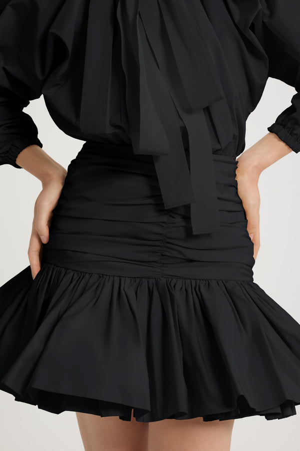 Patou - Robe courte à manches bouffantes en faille recyclée - Black - Robe en faille recyclée noire. Modèle court. Haut volumineux et bas ajusté. Col à coulisse avec détail de fronce et gros-grain. Manches chauve-souris resserrées aux poignets. Jupe froncée avec volant au bas. Fermeture par zip sur le côté.Cette robe fait partie de la collection Cérémonie créée pour les occasions spéciales.