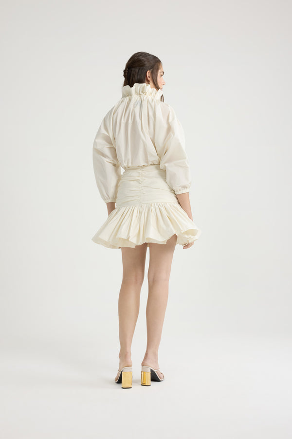 Patou - Robe courte à manches bouffantes en faille recyclée - Ivory - Robe en faille recyclée ivoire. Modèle court. Haut volumineux et bas ajusté. Col à coulisse avec détail de fronce et gros-grain. Manches chauve-souris resserrées aux poignets. Jupe froncée avec volant au bas. Fermeture par zip sur le côté.Cette robe fait partie de la collection Cérémonie créée pour les occasions spéciales.