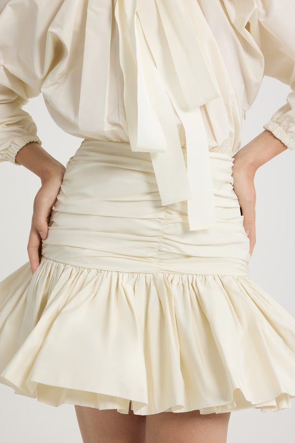 Patou - Robe courte à manches bouffantes en faille recyclée - Ivory - Robe en faille recyclée ivoire. Modèle court. Haut volumineux et bas ajusté. Col à coulisse avec détail de fronce et gros-grain. Manches chauve-souris resserrées aux poignets. Jupe froncée avec volant au bas. Fermeture par zip sur le côté.Cette robe fait partie de la collection Cérémonie créée pour les occasions spéciales.